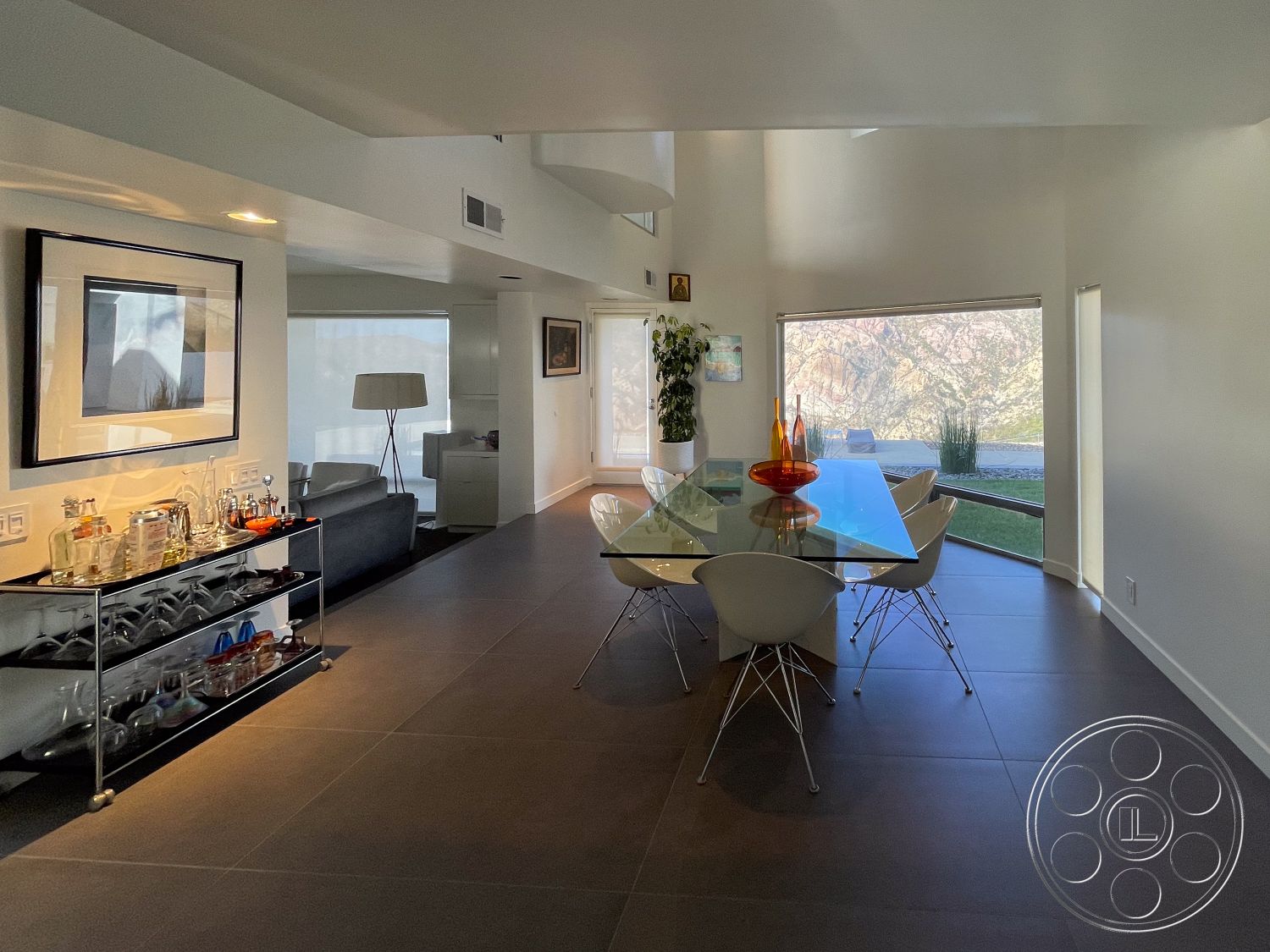 Modern 56 - high ceilings, minimalist design, contemporary decor, modern lighting fixtures, floor-to-ceiling windows, potted greenery, exposed ceiling, large glass dining table, open-plan living space, interior dining area, white painted walls, artwork wall decor, steel dining chairs, dark tile flooring, bar cart with glassware, natural light floods room, view of mountainous landscape, seamless indoor-outdoor integration