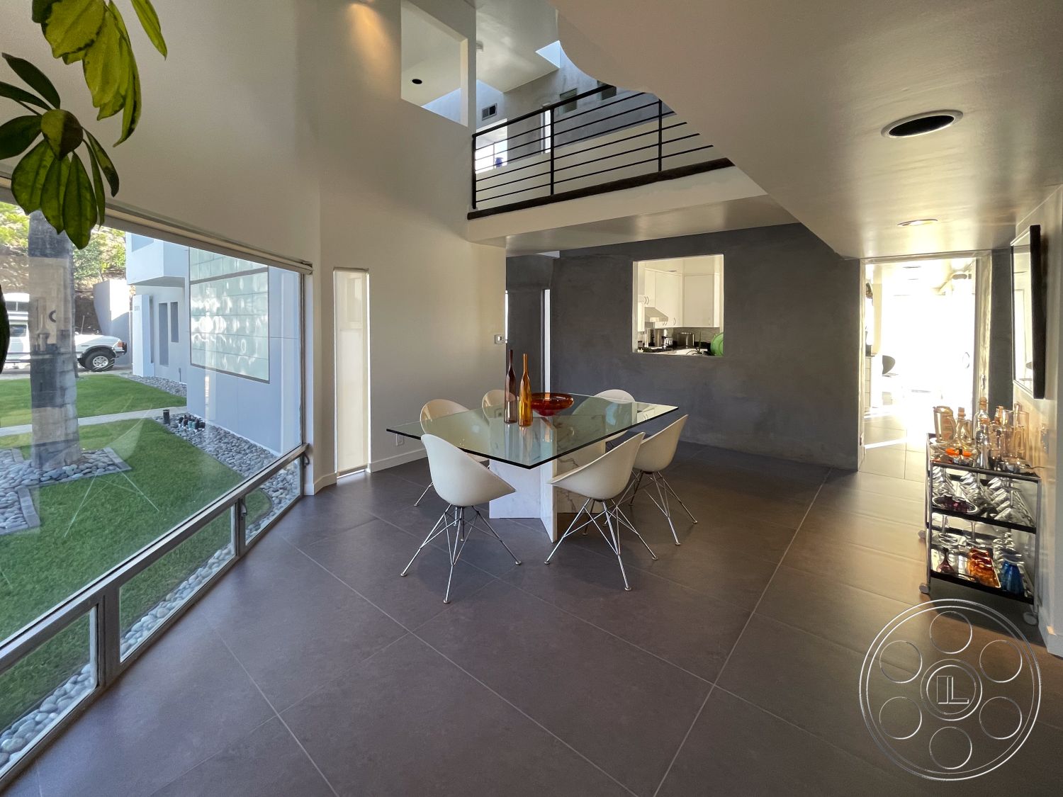 Modern 56 - minimalist aesthetic, modern light fixtures, open concept layout, floor-to-ceiling windows, glass dining table, interior dining area, smooth plaster walls, white plastic dining chairs, grey porcelain floor tiles, transom windows for natural light, stainless steel kitchen accents, steel railings on balcony, lush green landscaping visible through windows, urban setting with contemporary architecture