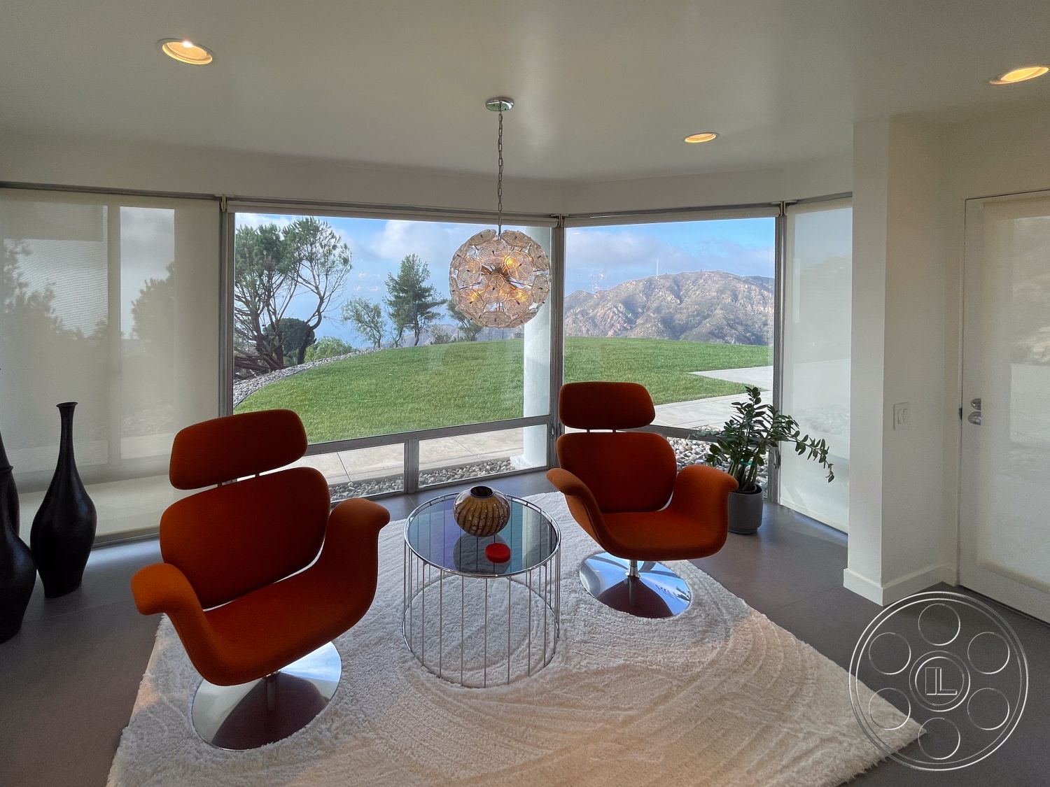 Modern 56 - minimalist decor, neutral wall colors, decorative vase, open floor plan, floor-to-ceiling windows, smooth concrete flooring, contemporary lighting fixture, natural light-filled space, indoor plant accent, suburban hillside location, interior modern lounge seating, orange upholstered lounge chairs, glass coffee table with metal frame, plush white area rug, scenic mountain view, exposed edges of the landscape outside