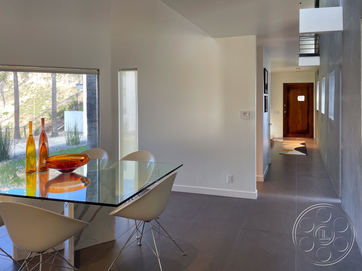 Modern 56 - natural wood front door, mid-century modern architectural style, minimalist hallway design, indoor plants for decor, interior polished concrete flooring, geometric shapes in furniture design, large windows with natural light, open floor plan kitchen and dining area, textured plaster wall accent, interior concrete wall finishes, glass dining table with marble base, modern dining chairs with chrome legs, sliding glass door with view to outdoor setting, exposed metal stair railings, neutral color palette with white walls, artistic glass bowl centerpiece, bright and airy interior atmosphere, strategic lighting fixtures for ambiance