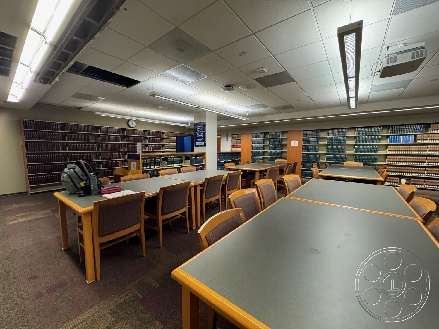 School 3 - carpet flooring, suspended ceiling tiles, fluorescent lighting fixtures, laminate study tables, wooden library chairs, built-in book shelves, neutral wall paints, rectangular study layout, large library space, academic study area