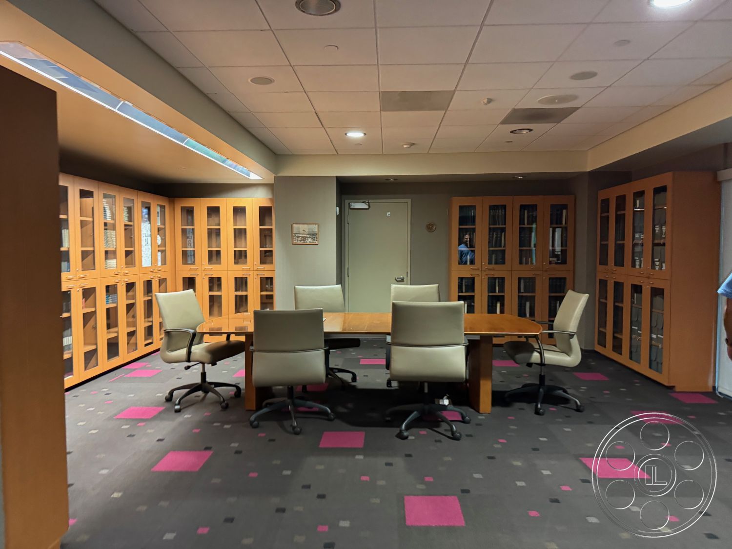 School 3 - glass display cabinets, recessed ceiling lights, neutral painted walls, interior office space, collaborative work environment, upholstered office chairs, private office setting, wooden cabinetry with glass doors, hardwood conference table, carpet flooring with geometric patterns, plush pink and gray carpet tiles, modern meeting room, dimmable ambient lighting