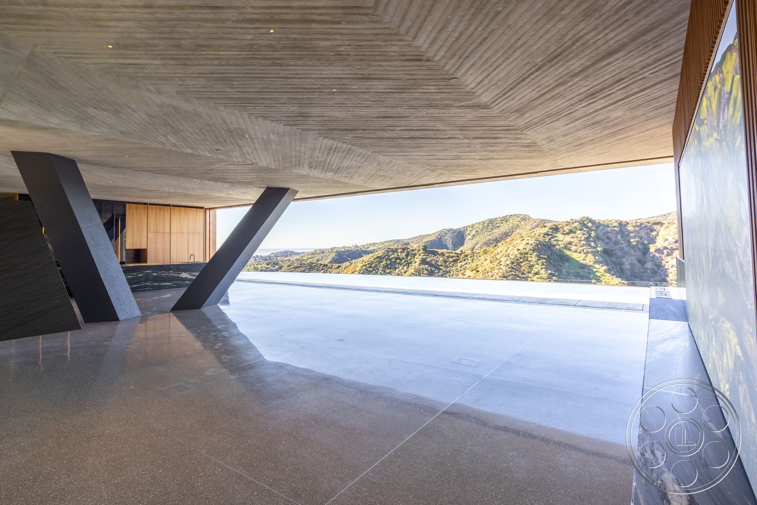 Modern 516 - open-air living space, mountain view setting, exposed wood ceiling beams, exterior concrete patio floor, floor-to-ceiling glass windows, minimalist architectural style, integrated indoor-outdoor living, interior wooden wall paneling, high ceiling interiors, interior concrete wall finish, exterior polished concrete surface, exterior concrete support columns, modern angular construction, contemporary outdoor area, large open floor plan