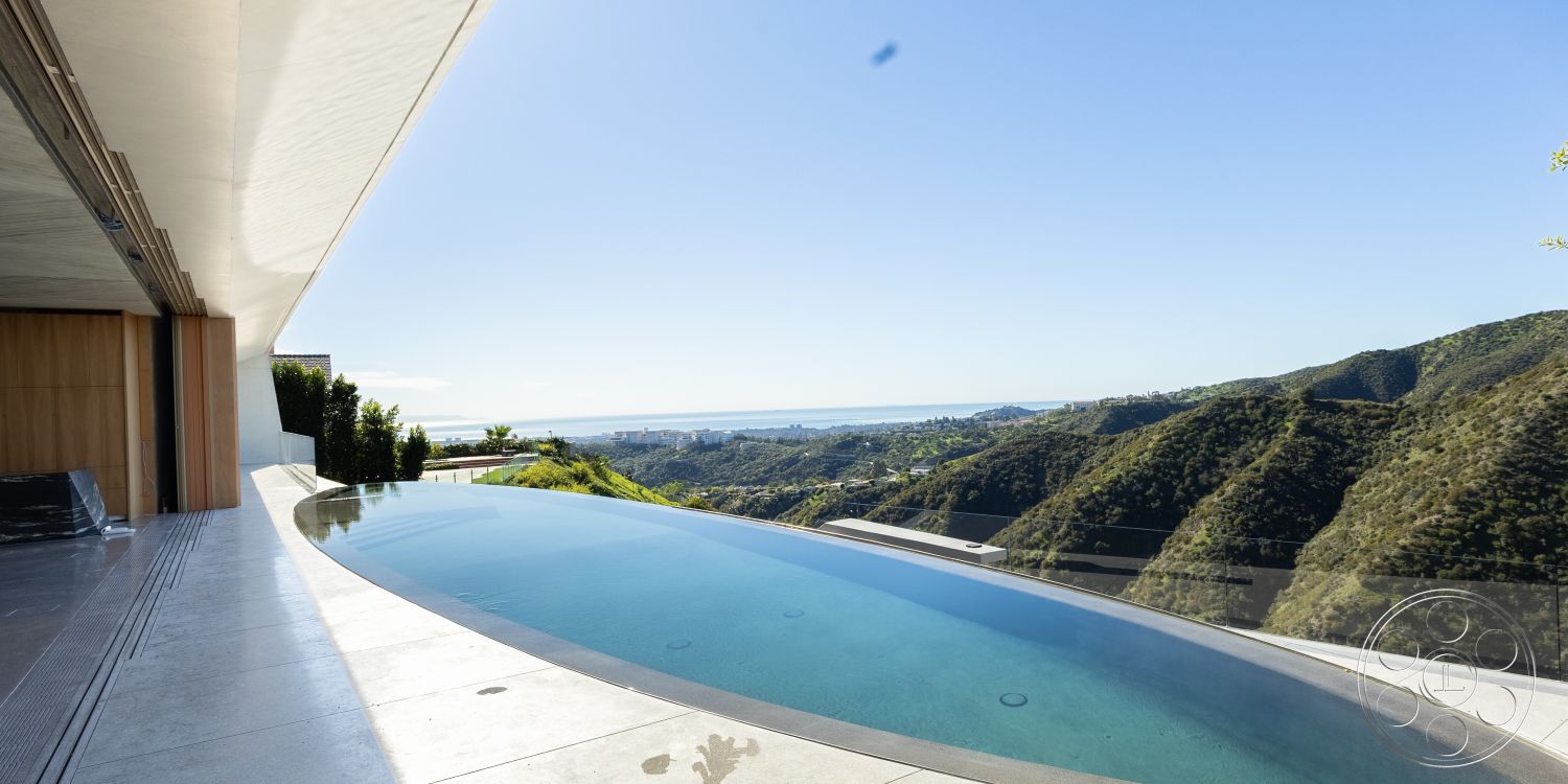 Modern 516 - glass railing, outdoor living space, modern architectural style, textured plaster walls, open-air patio, infinity pool, concrete pool deck, large sliding glass doors, sunny exterior setting, landscaped hillside garden, exterior limestone tiles, view of urban skyline, concrete overhang, ceiling-to-floor windows