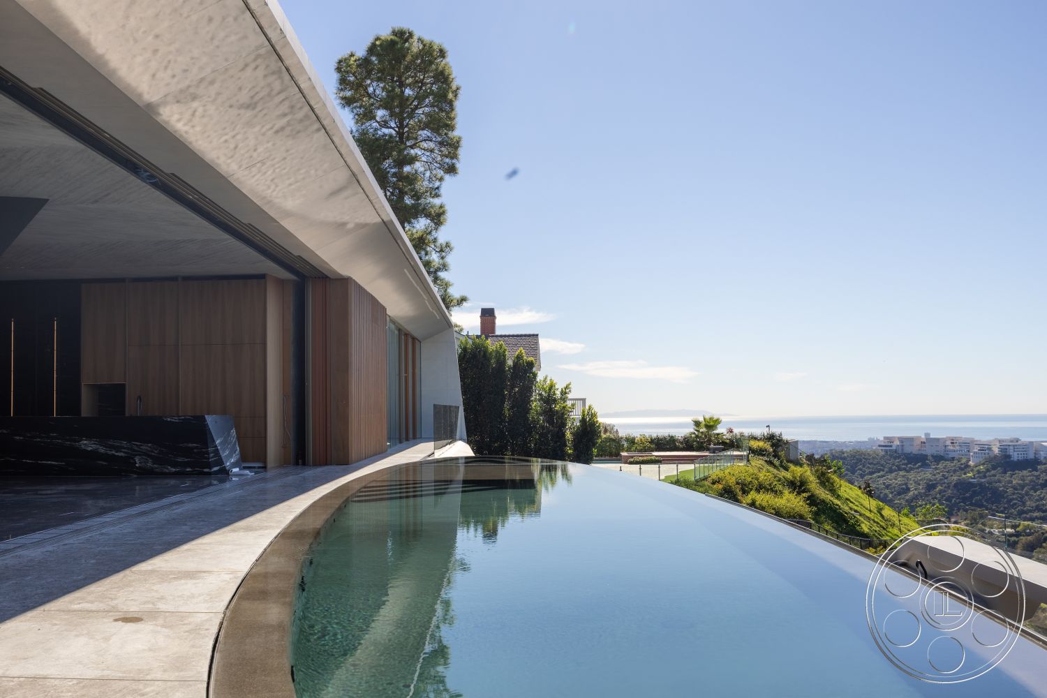 Modern 516 - exterior modern architectural design, exterior concrete infinity pool, exterior curved concrete patio floor, exterior glass railings overlooking hillside view, exterior wooden feature wall, exterior natural stone pool deck, exterior large floor-to-ceiling sliding glass doors, exterior lush landscaping with greenery, exterior gentle slope hillside location, exterior panoramic ocean view, exterior minimalistic design aesthetics, exterior integrated outdoor living space, exterior smooth concrete roof overhang