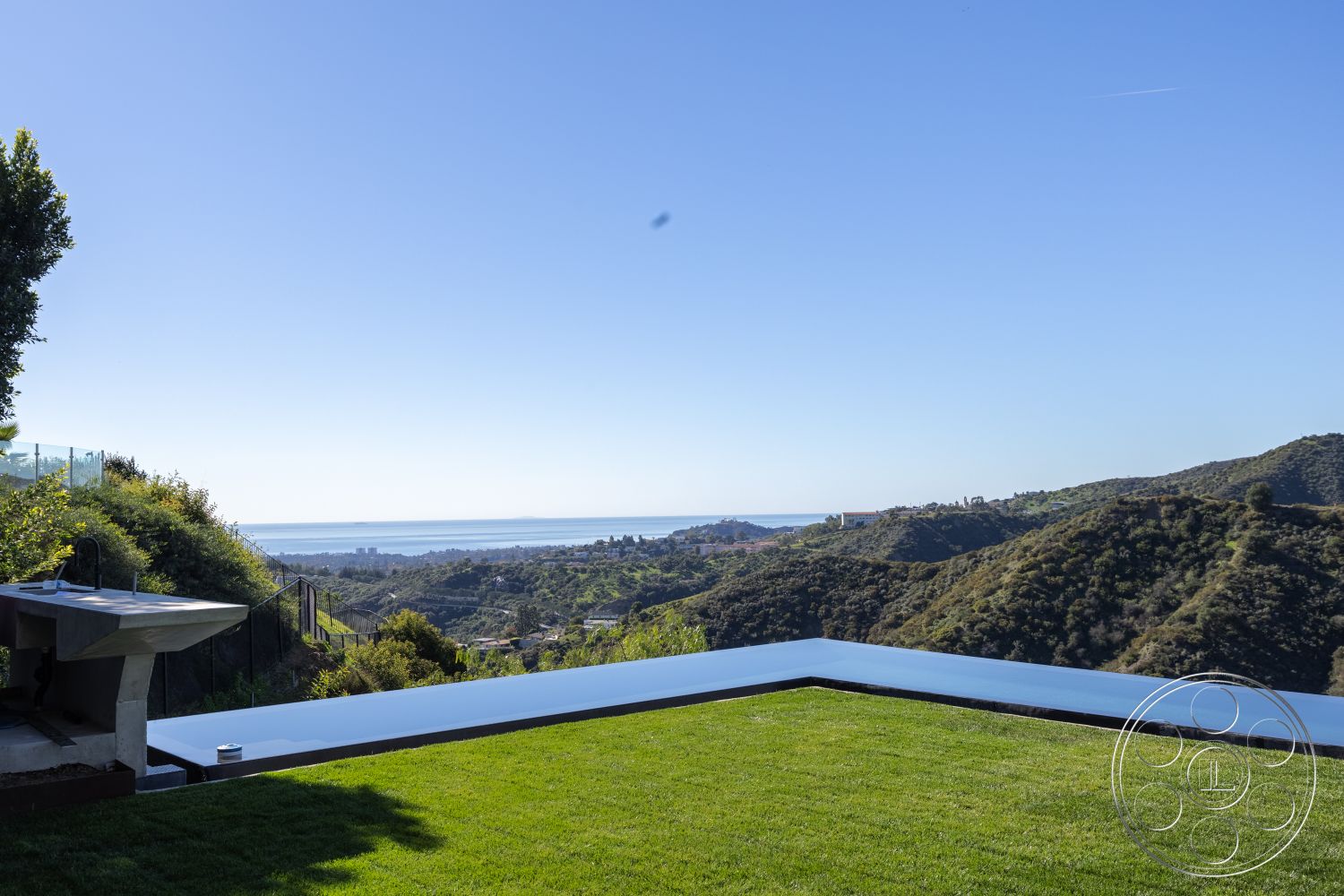 Modern 516 - glass railing, open-air environment, concrete pool deck, mountain view setting, minimalist patio design, stainless steel outdoor grill, contemporary backyard, grass lawn area, modern outdoor living space, exterior infinity pool with reflective surface, landscaped hillside terrace, coastal skyline, natural hillside vegetation, sun-drenched outdoor area