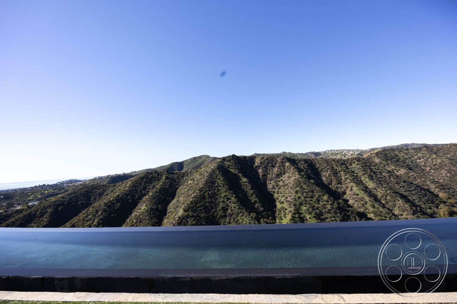 Modern 516 - exterior, seamless indoor-outdoor transition, outdoor living space, clear blue sky, natural setting, lush greenery surrounding, modern architectural design, mountain view backdrop, contemporary home exterior, infinity pool edge, black stone pool deck, landscape with rolling hills, smooth water surface