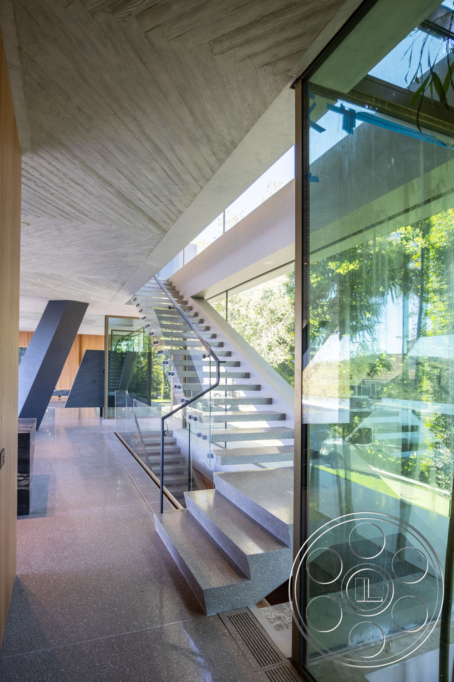Modern 516 - minimalist aesthetic, polished concrete flooring, seamless indoor-outdoor transition, floor-to-ceiling windows, open concept living space, exposed concrete ceiling, architectural simplicity, contemporary interior, elevated living area, glass partition walls, modern architectural design, natural light infiltration, wood panel accent wall, geometric shapes in design, sculptural staircase design, terrazzo floor finish, floating stairs with glass railing, interior foyer with natural light, wood beam structural elements, lush indoor plants view