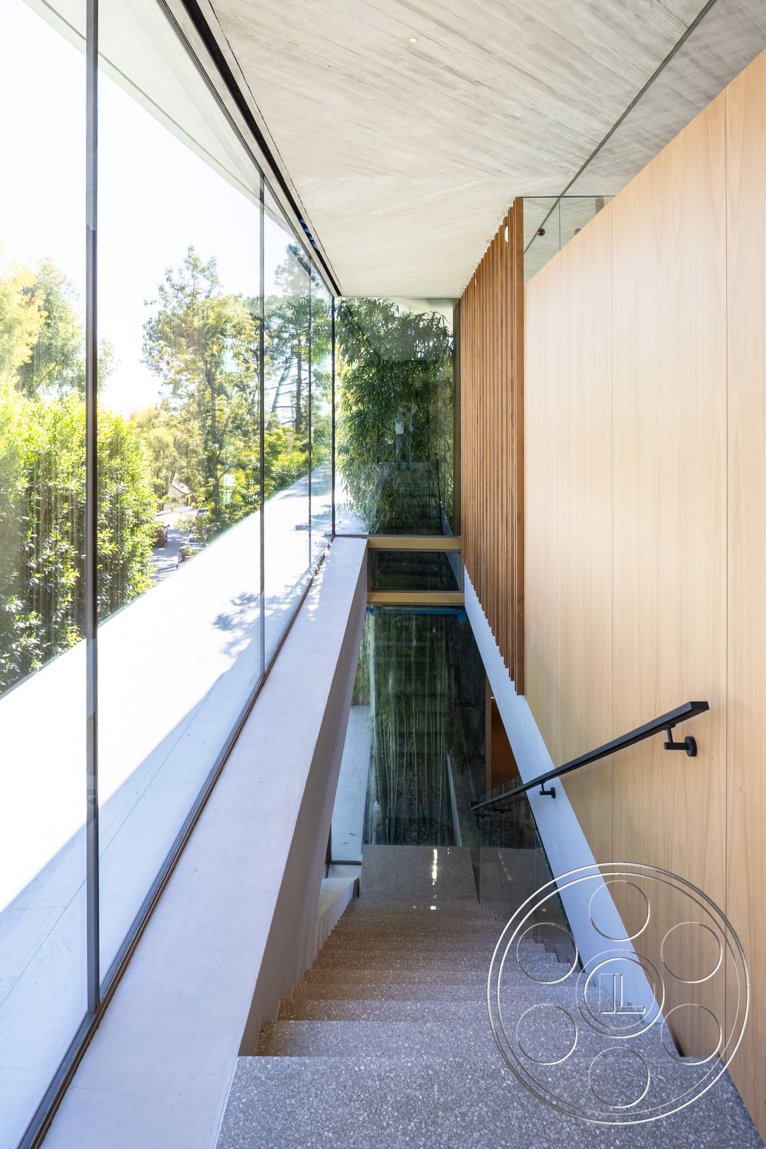 Modern 516 - open concept layout, seamless indoor-outdoor transition, exposed concrete ceiling, clear glass partitions, minimalist architectural design, wood panel accent wall, natural light maximization, interior glass wall systems, terrazzo stair treads, glass railing staircases, framed view of lush greenery, linear staircase design, modern interior architecture, horizontal wood slats for privacy, stairwell with integrated lighting