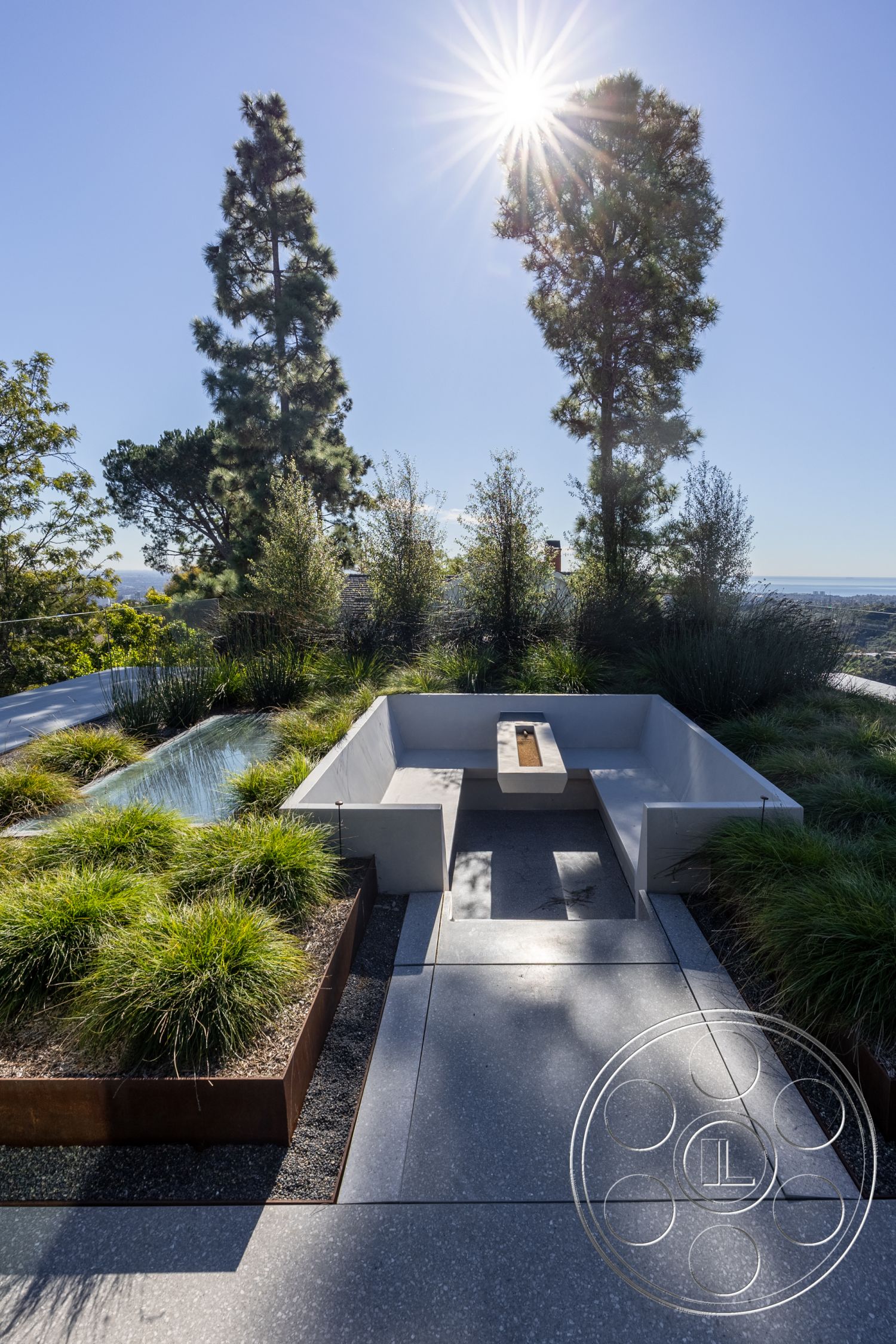 Modern 516 - tall evergreen trees, linear water feature, minimalist outdoor design, sunny hillside location, exterior concrete patio flooring, exterior polished concrete seating area, rectangular garden bed, rusted Corten steel planters, lush ornamental grass landscaping, modern landscape architecture