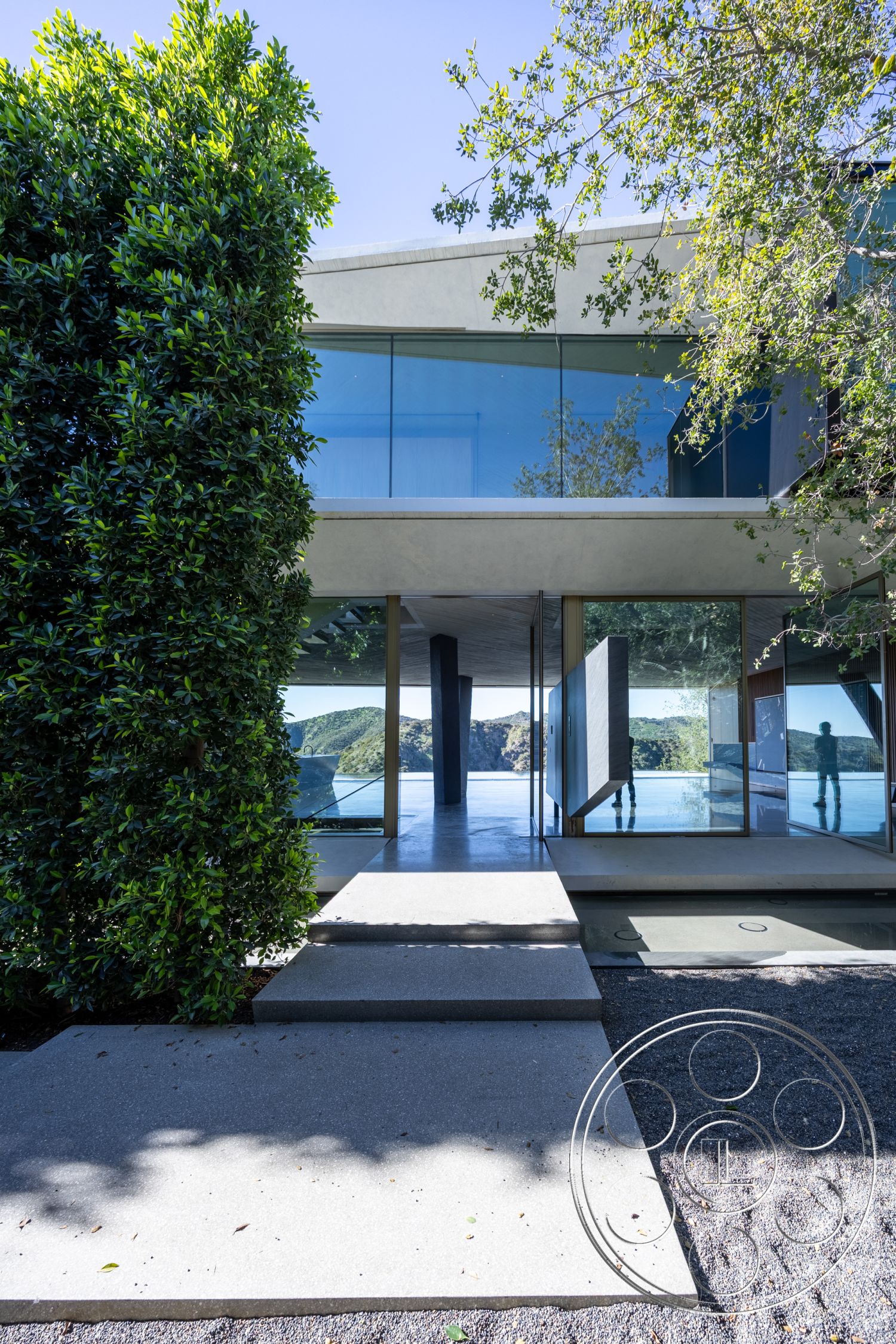 Modern 516 - exterior, lush greenery, minimalist aesthetic, open floor plan, floor-to-ceiling windows, glass facade, contemporary design elements, modern architectural style, gravel landscaping, concrete walkway, metal framing, flat roof design, stone landscape features, skylight elements, surrounding mountains view, transitional indoor-outdoor space