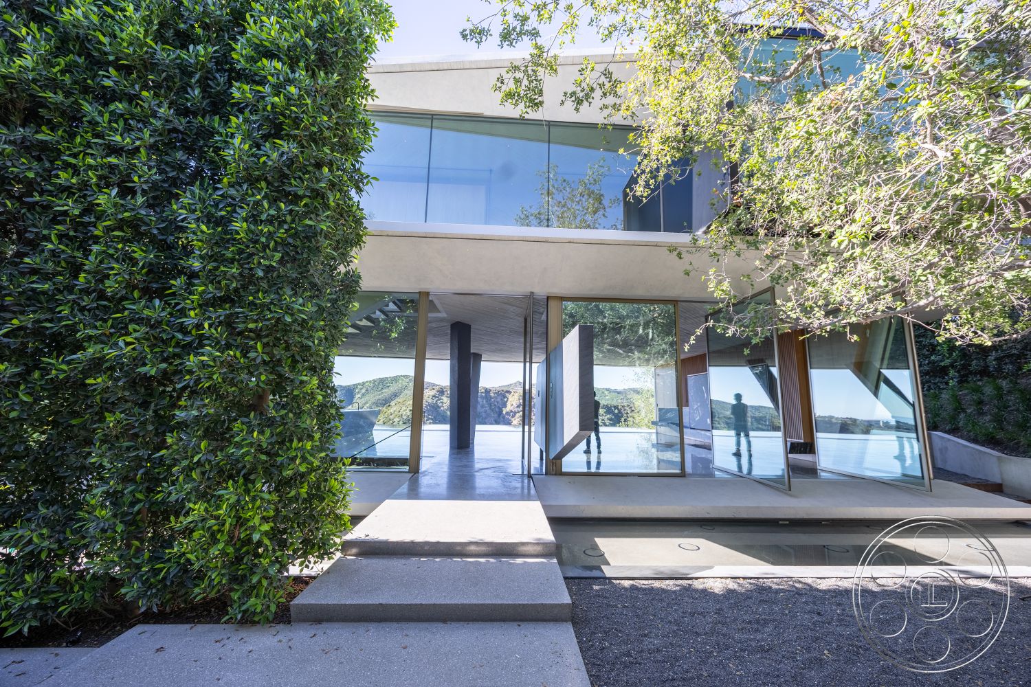 Modern 516 - minimalist design elements, smooth concrete surface, modern architectural style, contemporary outdoor space, integrated landscaping, open-plan layout, concrete patio flooring, exterior concrete walls, wood accent features, glass floor-to-ceiling windows, reflective glass surfaces, concrete steps leading to entrance, landscape design with lush greenery, geometric shapes in structure, natural setting with mountain view, shadow play from overhanging roof, asymmetrical roof structure, surrounding nature blend