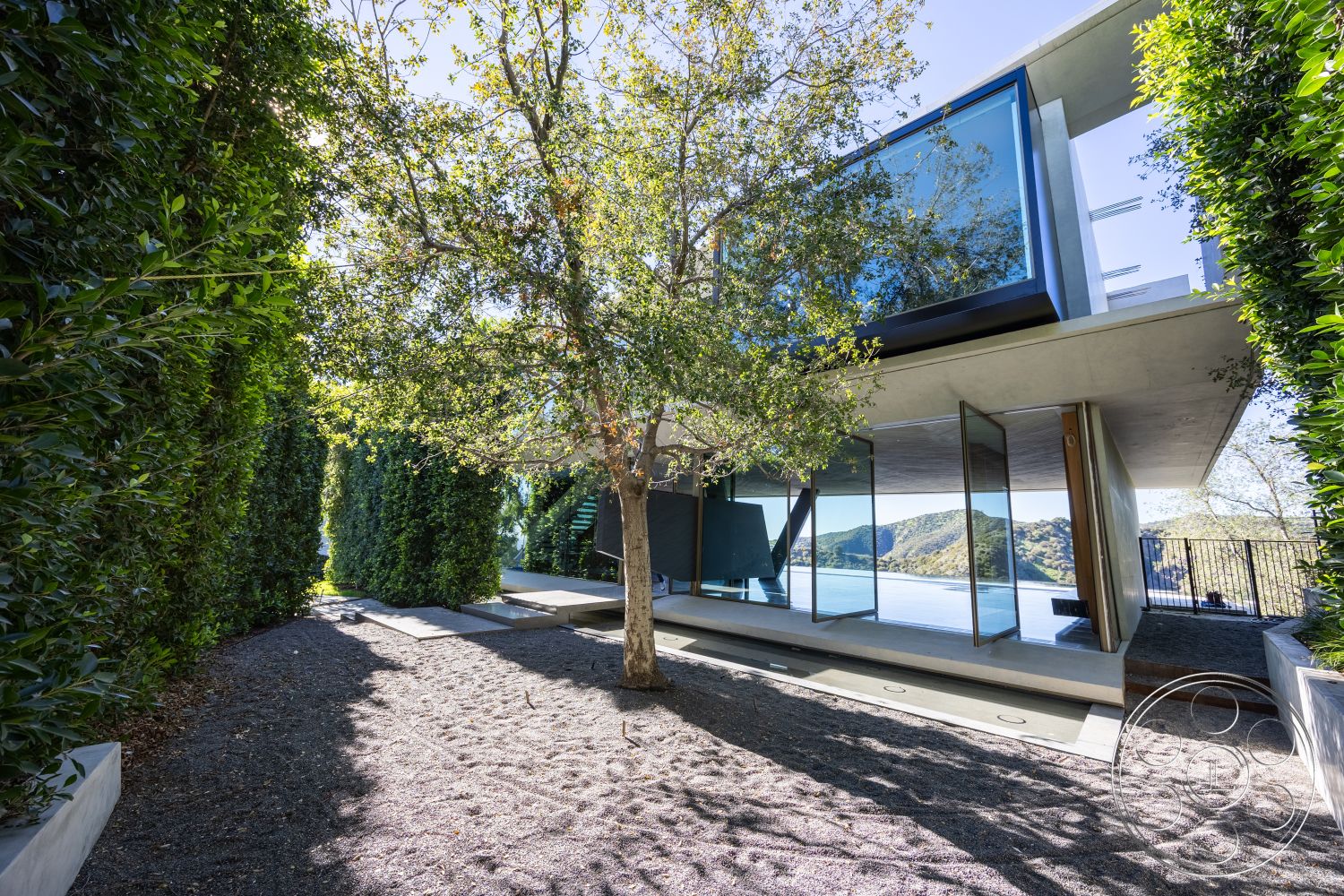 Modern 516 - outdoor living space, open-air design, lush green hedges, concrete terrace, modern outdoor space, elevated construction, contemporary architectural style, natural light emphasis, minimalist design aesthetics, glass floor-to-ceiling windows, sustainable materials usage, serene nature setting, natural stone landscaping, exterior concrete structural elements, wood beam details, landscaped gravel pathway, surrounding hillside environment, floating concrete steps, scenic lakefront view, architectural cantilever