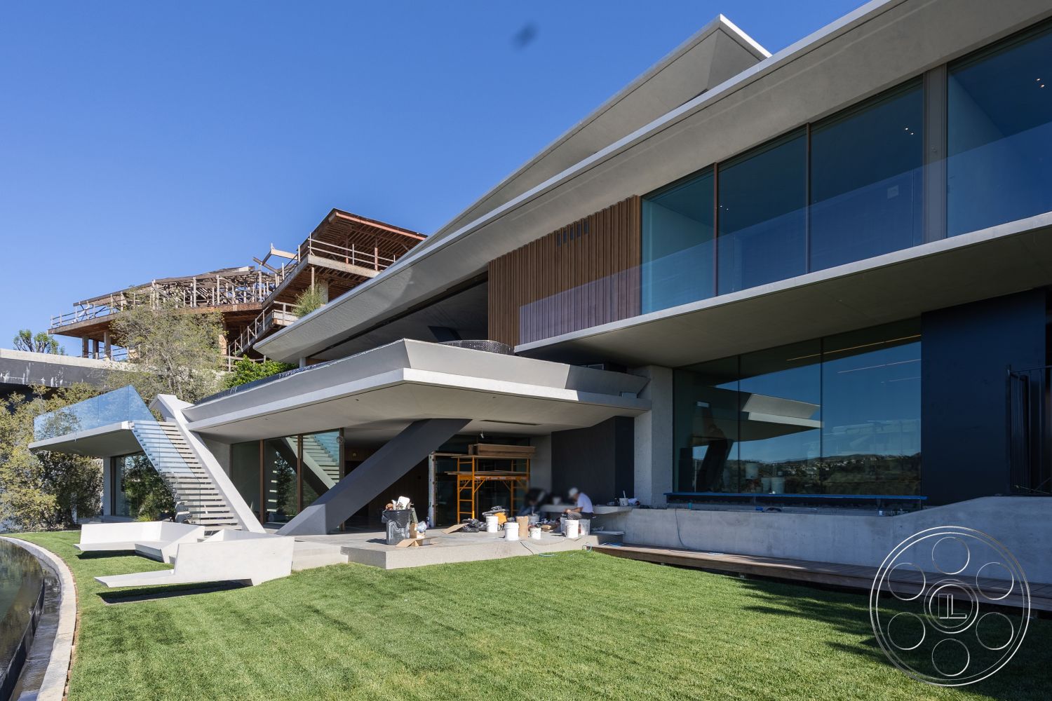 Modern 516 - concrete patio, contemporary design elements, modern architectural style, mountain view, stainless steel finishes, flat roof design, interior open floor plan, exterior concrete walls, floor-to-ceiling glass doors, steel stair railings, urban hillside setting, exterior glass windows, interior vaulted ceilings, landscaped grassy area, exposed concrete foundation, exterior wooden slat panels, rectangular concrete steps, cut stone landscaping borders, geometric feature elements, construction scaffolding in background