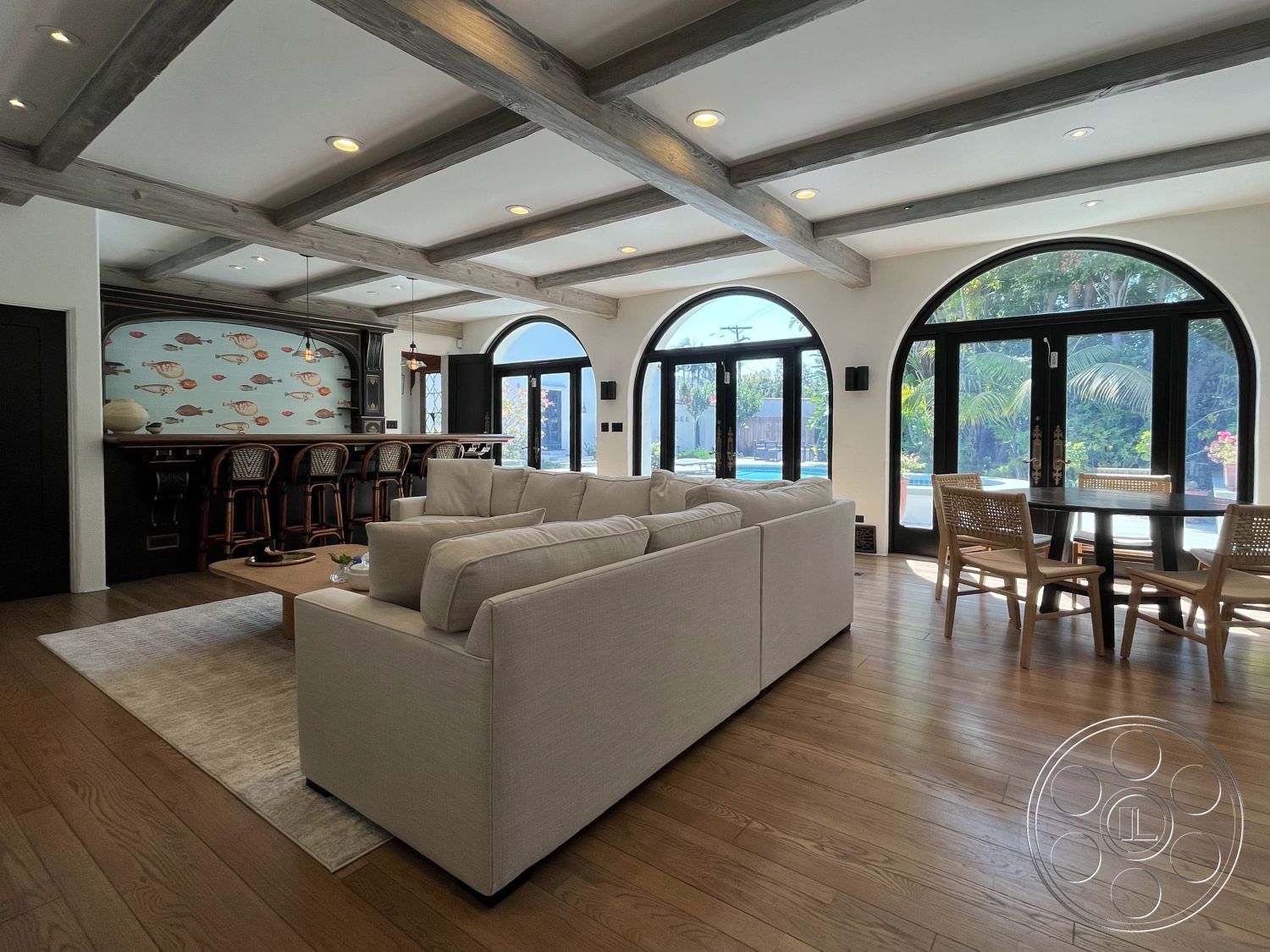 Medit 166 - cozy seating arrangement, casual dining space, contemporary coffee table, black framed glass doors, exposed wood ceiling beams, interior hardwood living room floors, open floor plan layout, arched window openings, beach house setting, chic bar area with wooden stools, lightly textured wall finish, modern upholstered sectional sofa, abstract fish wallpaper