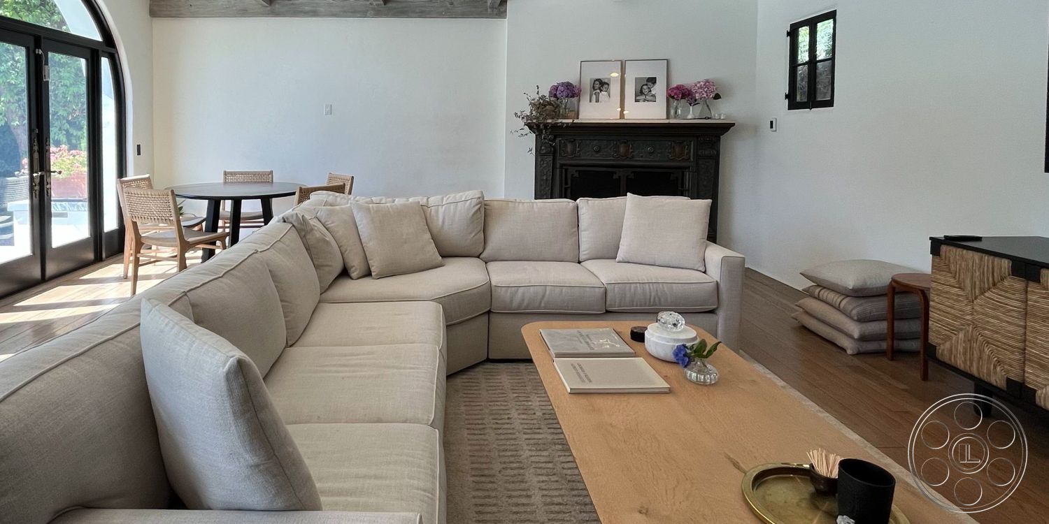 Medit 166 - contemporary design elements, soft natural lighting, exposed wood ceiling beams, white painted walls, interior sectional sofa, open-plan living area, decorative flower arrangements, light-colored fabric upholstery, wood coffee table with natural finish, dark wood fireplace mantel, neutral area rug with geometric pattern, round dining table with natural wood finish, woven dining chairs with armrests, large glass doors leading to outdoor space, minimalist wall decor with framed art prints, warm hardwood flooring, relaxed, inviting atmosphere