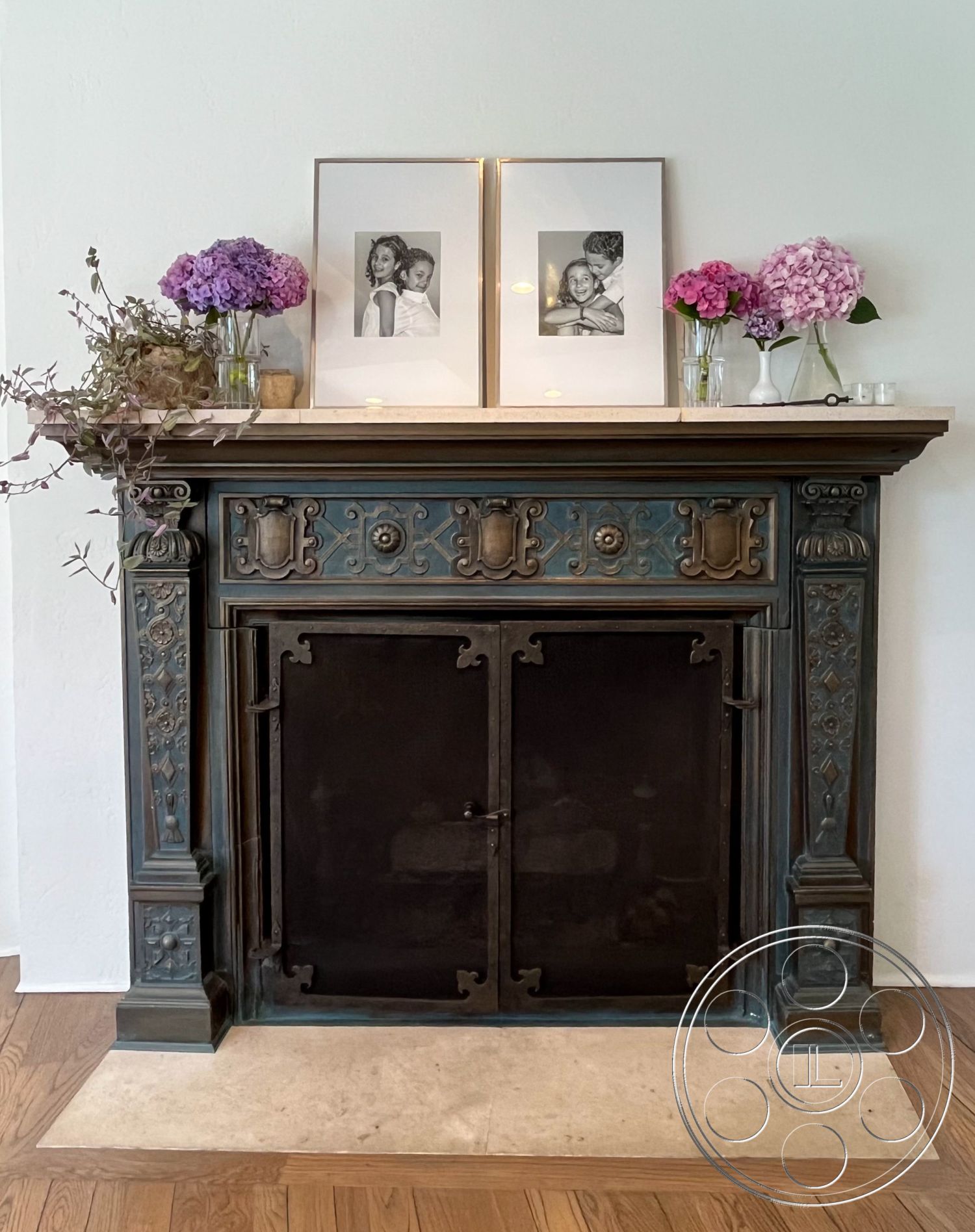 Medit 166 - light hardwood flooring, neutral wall paint, exposed brick wall accent, natural wood trim details, interior fireplace mantel, ornate cast iron fireplace surround, wood mantel shelf, photographs in gold frames, fresh hydrangea flower arrangements, decorative floral display, subtle textured plaster wall treatment