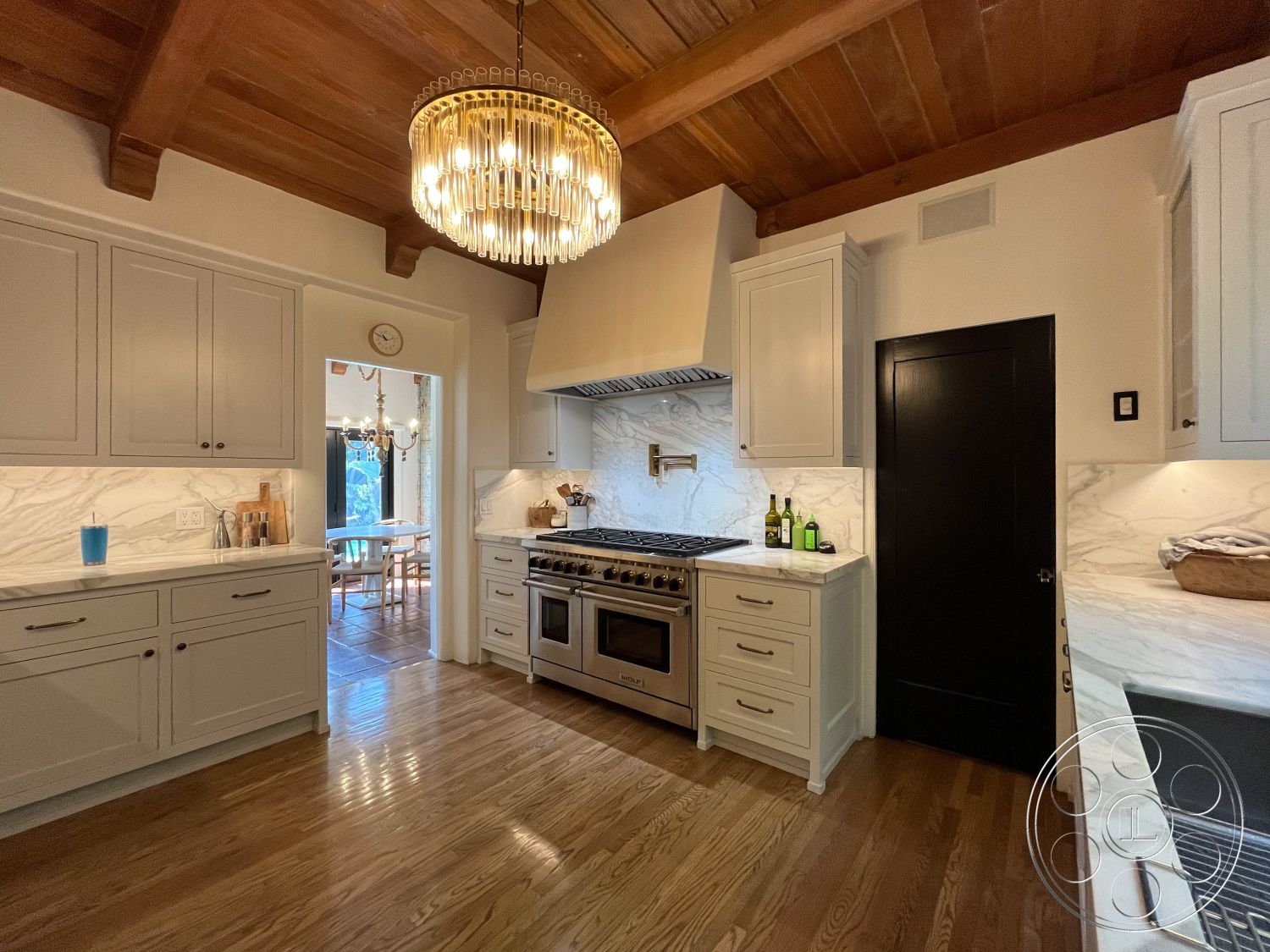 Medit 166 - exposed wood ceiling beams, interior kitchen with hardwood flooring, neutral color palette with warm wood tones, functional chef's kitchen, marble backsplash with white cabinets, granite kitchen countertops with stainless steel appliances, black door accents, open floor plan with a view to dining area, modern kitchen lighting fixture, elegant kitchen design with polished finishes, single-handle kitchen faucet