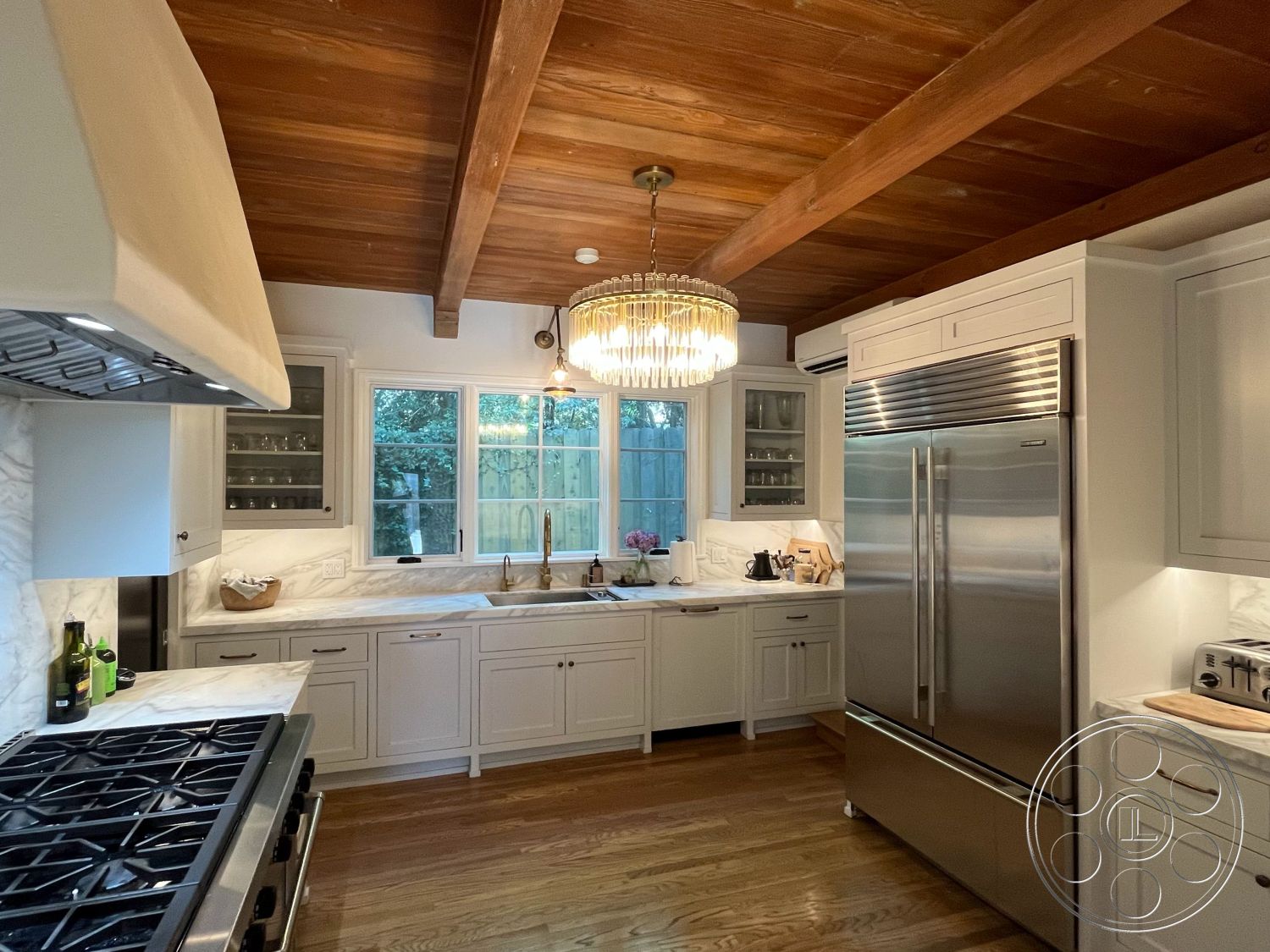 Medit 166 - suburban setting, stainless steel refrigerator, neutral color scheme, decorative backsplash, exposed wood ceiling beams, marble kitchen countertops, open kitchen layout, stainless steel gas range, hardwood kitchen floors, natural light exposure, glass kitchen window, home chef's kitchen, modern kitchen lighting fixture, white painted cabinets, glazed ceramic sink