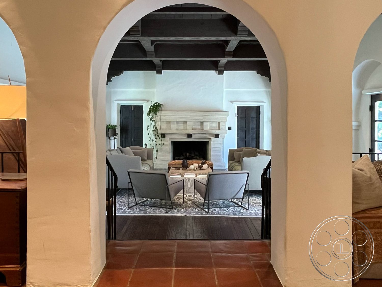 Medit 166 - open floor plan, indoor-outdoor flow, arched doorways, minimalist coffee table, terracotta tile flooring, wood-framed windows, area rug with geometric patterns, interior living room, vaulted ceiling with exposed wood beams, stone fireplace surround, plaster wall finishes, neutral fabric upholstered chairs, built-in bookcase, decorative plants in pots, traditional wooden door