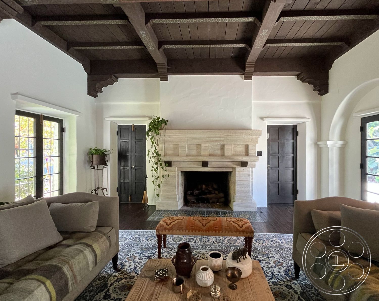 Medit 166 - neutral color palette, decorative area rug, arched doorways, mid-century modern furniture, indoor plant decor, black wooden door, exposed wood ceiling beams, interior living space, hardwood flooring in living room, stone fireplace surround, vaulted living room ceiling, white textured plaster walls, large windows with natural light, central fireplace feature, accent seating with patterned fabric