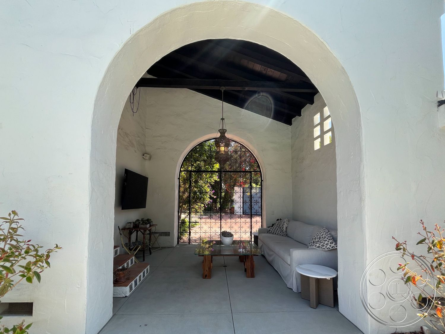 Medit 166 - outdoor living space, arched entryway, minimalist coffee table, exposed wood ceiling beams, concrete patio flooring, exterior stucco walls, suburban backyard setting, textured plaster wall treatment, contemporary outdoor seating area, glass door system, decorative wrought iron gate, shade from surrounding greenery, sunlit courtyard view