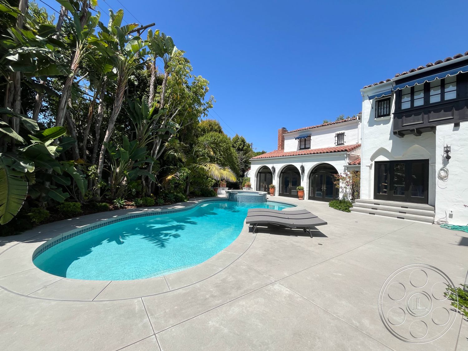 Medit 166 - exterior, arched doorways, residential backyard, concrete pool deck, wooden patio furniture, modern Mediterranean architecture, poolside lounge area, red tiled roof, sunny outdoor atmosphere, oval swimming pool, stucco house exterior, landscaped garden borders, modern outdoor living space, surrounding tropical landscaping, multi-level outdoor seating, private swimming area, patio with concrete finishes, potted plants lining pathways