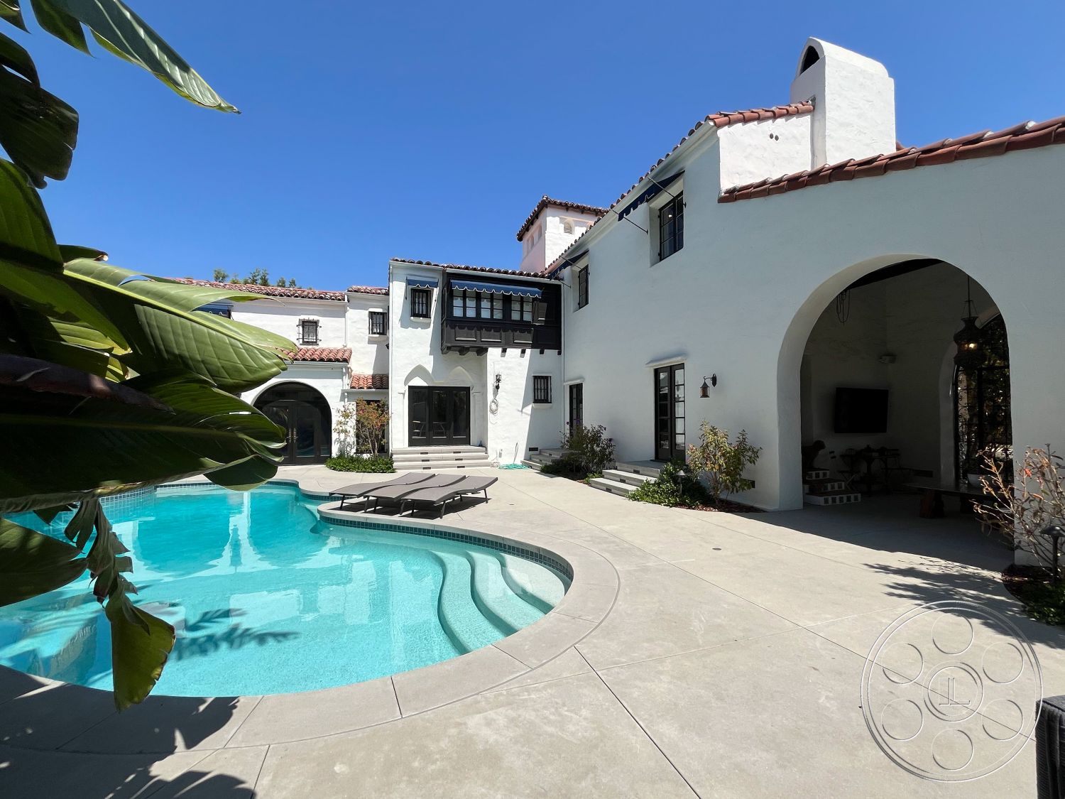 Medit 166 - exterior, white stucco walls, low-maintenance landscaping, sliding glass doors, arched doorways, Spanish tile roof, outdoor dining space, rectangular pool, poolside lounge area, outdoor water feature, concrete patio flooring, succulent garden accents, courtyard home, desert climate setting, black window trim, sunbathing deck, decorative wrought iron details, northwest-facing backyard, natural stone pool coping