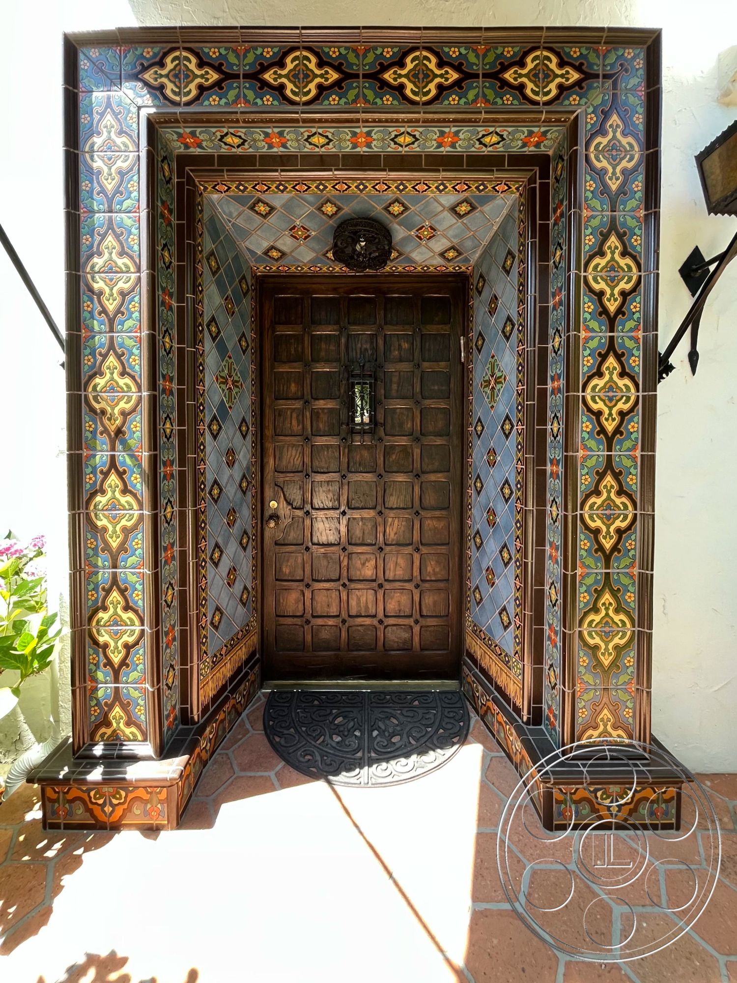 Medit 166 - textured plaster wall treatment, Mexican tile entryway, colorful decorative tiled archway, handcrafted wooden front door, ornate iron door handle, hexagon-shaped terracotta floor tiles, intricate tile patterns, exposed wood framing details, dark wood door with paneling, rustic tile border design, decorative tile inlay accents, antique-style light fixture, exterior entrance area, architectural detailing in entryway, vibrant mosaic tile work, inviting front door entrance