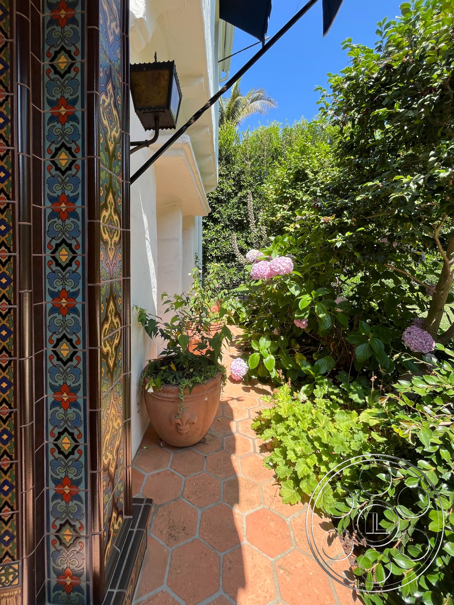 Medit 166 - textured plaster wall, outdoor garden setting, lush greenery landscape, tropical garden environment, terracotta pathway tiles, decorative ceramic tile accent wall, planter with hydrangeas, outdoor lantern light fixture, hexagonal patio flooring, exterior wall with painted stucco finish
