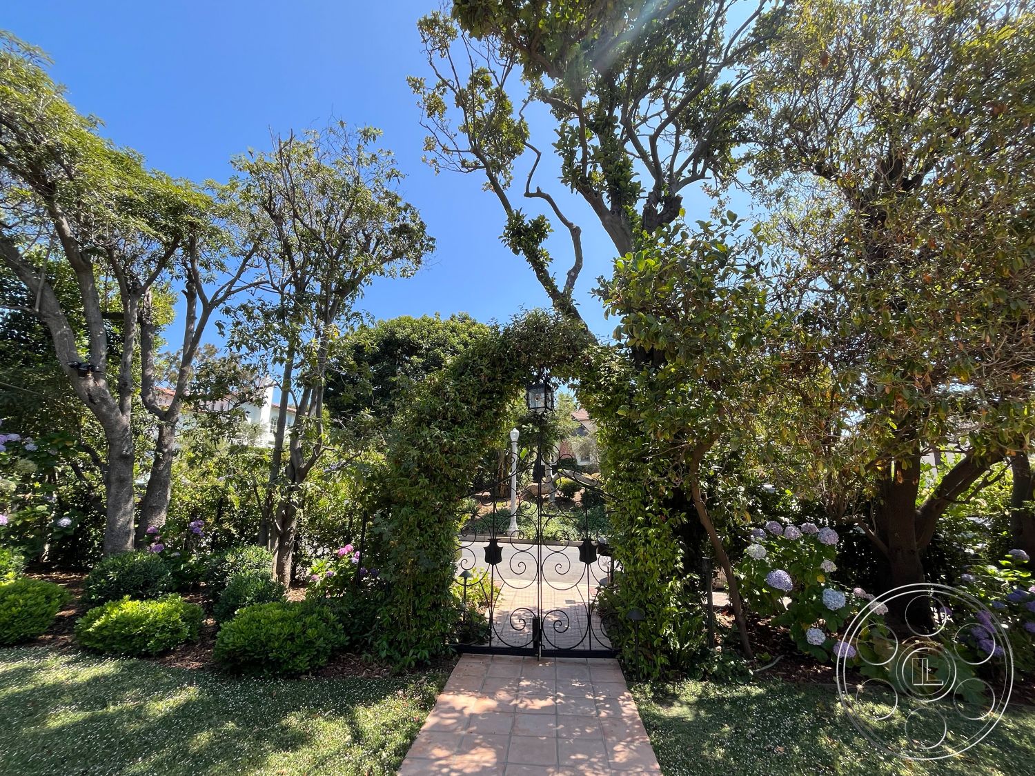 Medit 166 - mature trees, outdoor living space, flowering shrubs, formal garden design, textured stone pathway, lush green landscaping, softscape elements, suburban garden, sunny outdoor environment, symmetrical garden layout, seasonal flowering plants, interior garden pathway, wrought iron gate entrance, arched garden trellis, brick paver walkway, decorative garden lanterns