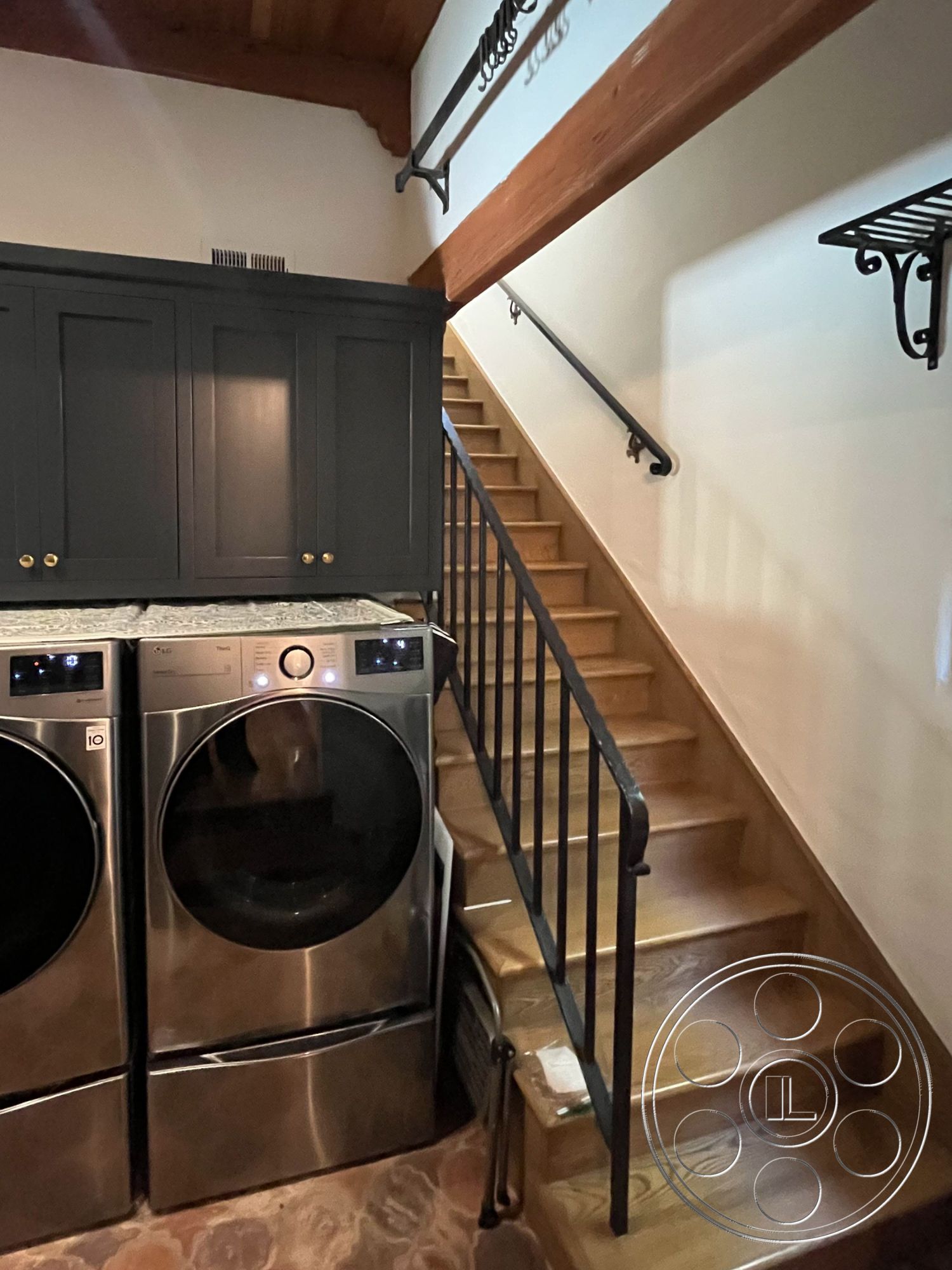 Medit 166 - dark wood cabinetry, textured stone flooring, black metal stair railing, open staircase design, floating wooden staircase, interior laundry room, stainless steel washer and dryer, vaulted wood ceiling beams, modern laundry area layout, minimalistic storage solutions