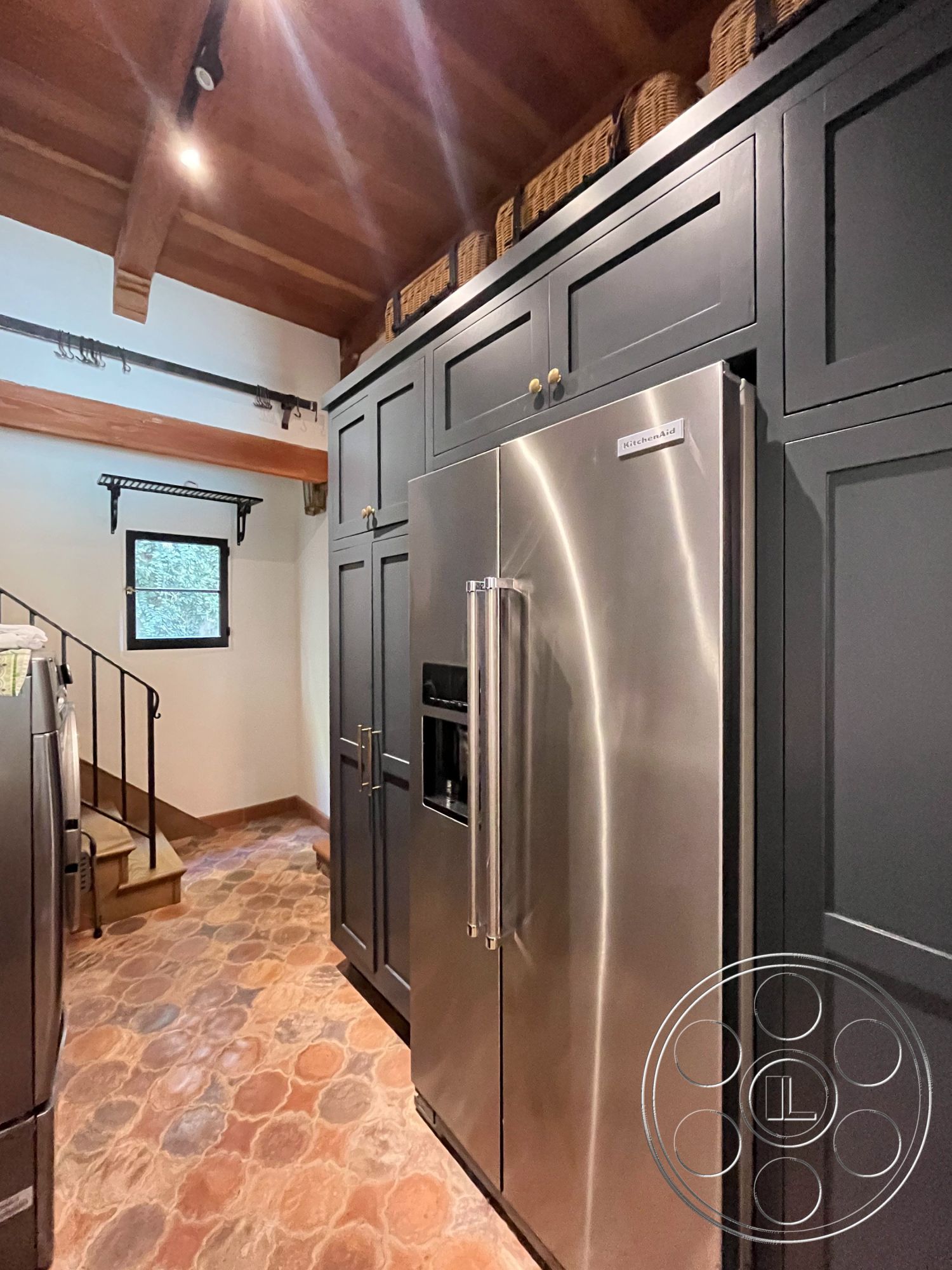 Medit 166 - spiral staircase, textured plaster walls, stainless steel refrigerator, modern rustic design, stone tile flooring, exposed wood ceiling beams, open kitchen layout, interior kitchen, black kitchen cabinets, farmhouse-style kitchen