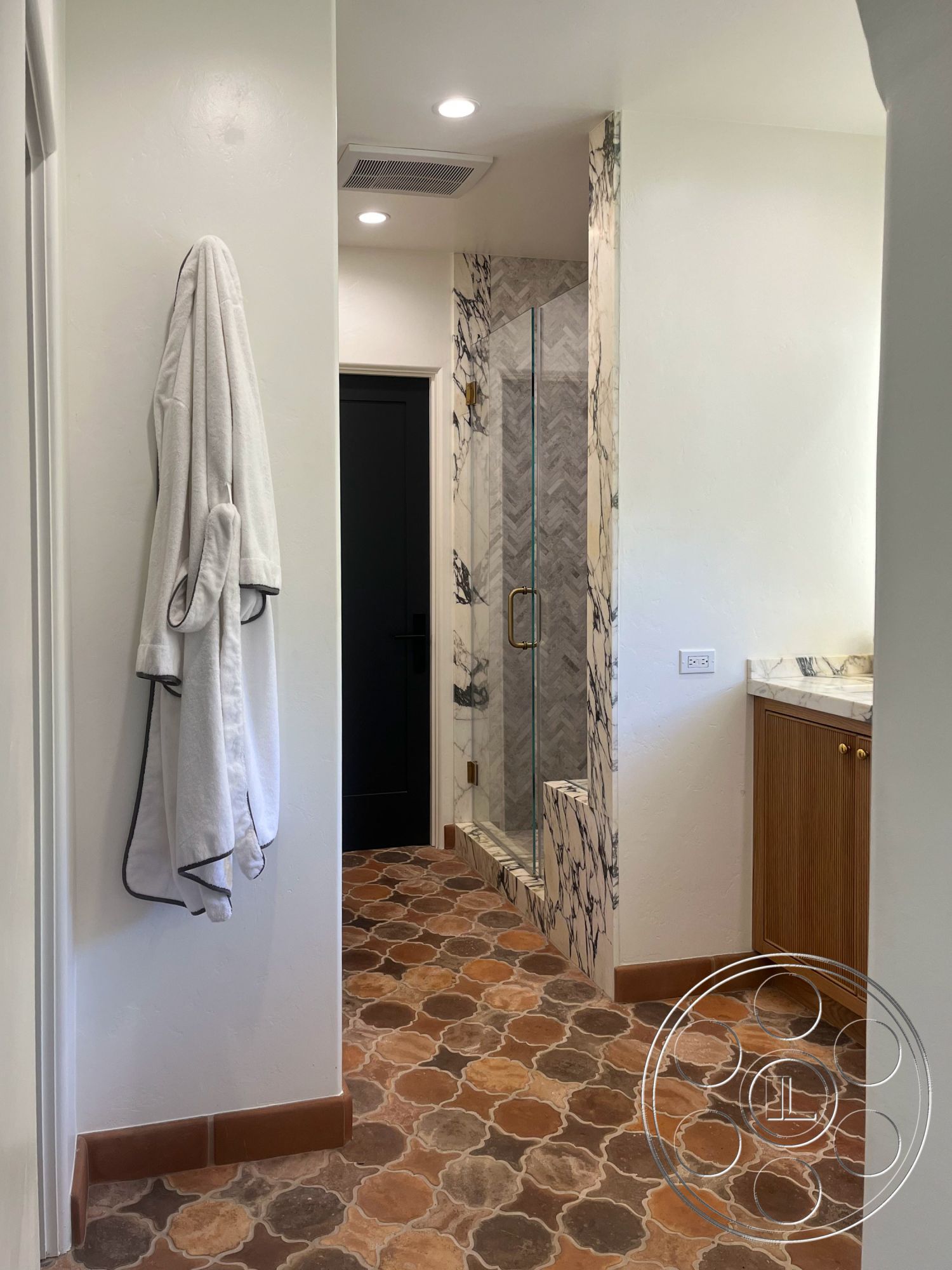 Medit 166 - neutral color palette, natural light, glass shower enclosure, marble countertop, soft lighting fixtures, textured plaster wall, interior bathroom, white painted walls, gold hardware details, handmade terracotta tile flooring, herringbone marble shower wall, wall-mounted vanity cabinet, dark wooden cabinet doors, sliding black door, luxurious robe hanging