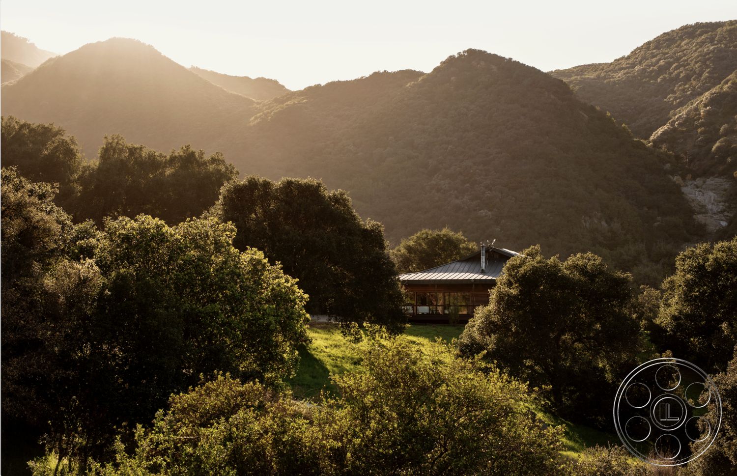 Topanga Retreat - wooden deck, open concept living space, natural stone pathway, large floor-to-ceiling windows, sustainable building materials, rustic cabin style, exterior wood paneling, modern architectural design, landscaped grassy area, metal roof overhang, surrounded by mountainous terrain, curved building shape, single-story residence, integration with natural surroundings, outdoor gathering area