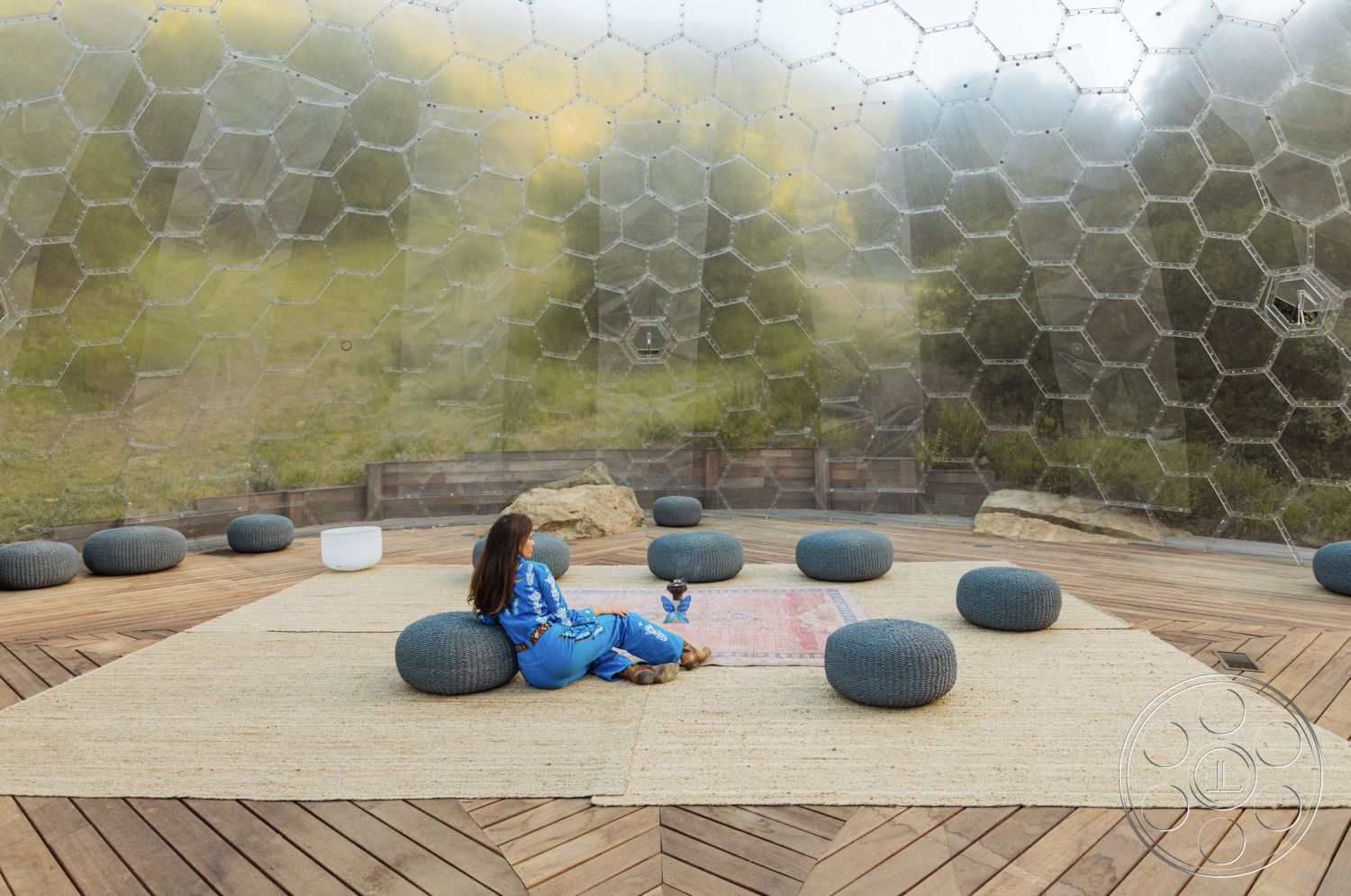 Topanga Retreat - minimalist design elements, woven natural fiber rug, wooden deck flooring, natural light-filled space, contemporary outdoor living space, textured wall details, stone landscaping features, hexagonal glass wall structure, circular outdoor seating, open-air interior, scenic mountain backdrop, eco-friendly architectural design, organic material palette, interior relaxation area