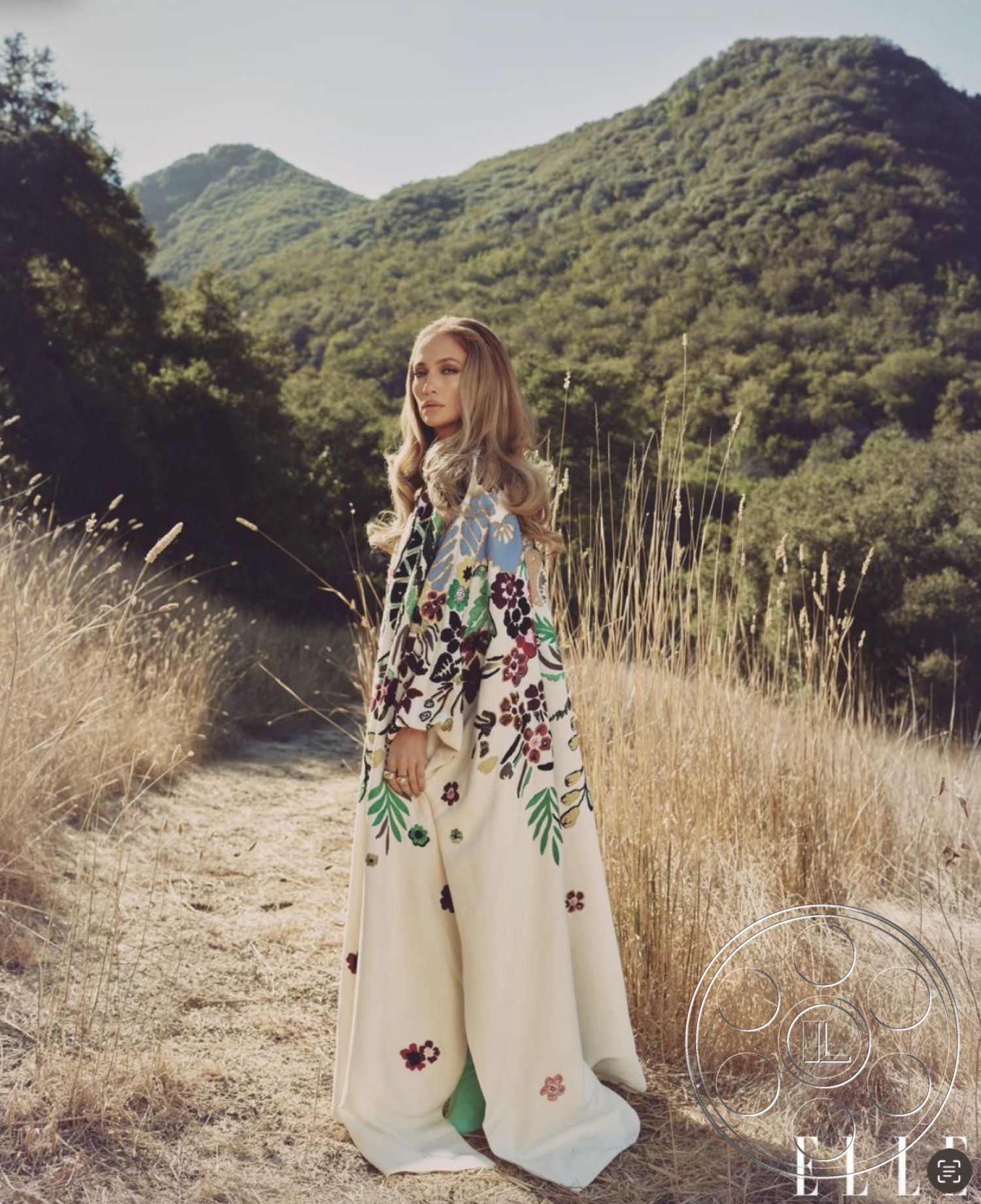 Topanga Retreat - mountain backdrop, natural setting, soft fabric, earth tone colors, sunlit pathway, casual outdoor style, outdoor location, tall dry grass, floral patterned garment, elegant dress, flowing silhouette