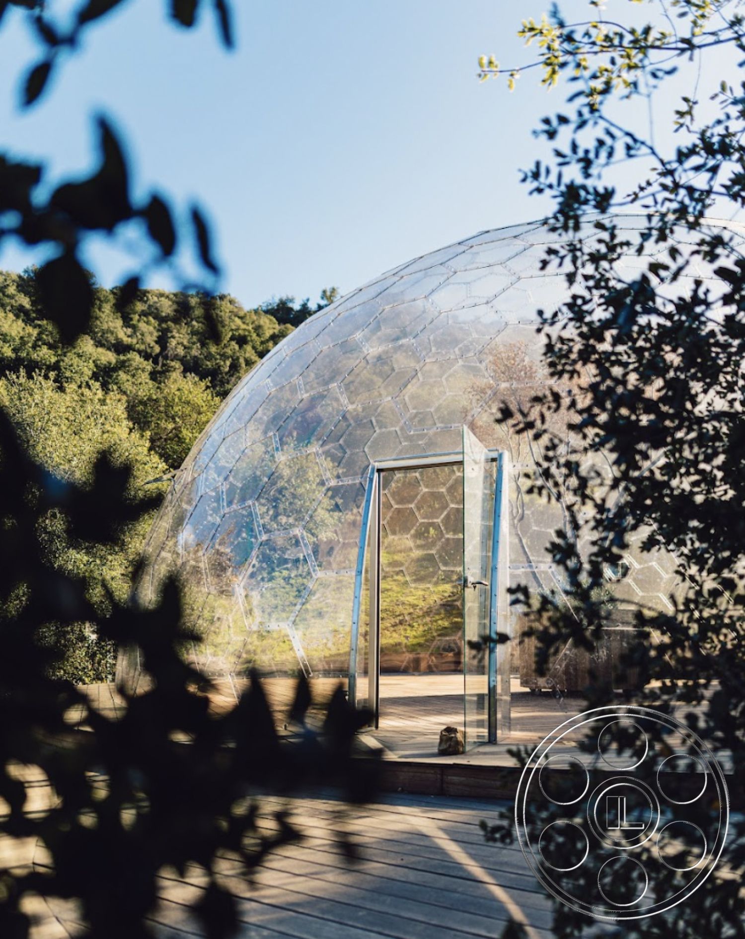Topanga Retreat - sliding glass door, wooden deck flooring, modern minimalist style, open concept interior, interior outdoor living space, hexagonal glass dome structure, transparent acrylic panels, natural woodland setting, sustainable architecture design, geodesic dome, environmentally integrated structure, scenic view patio, matérial contrast glass and wood, biodiversity enhancing environment