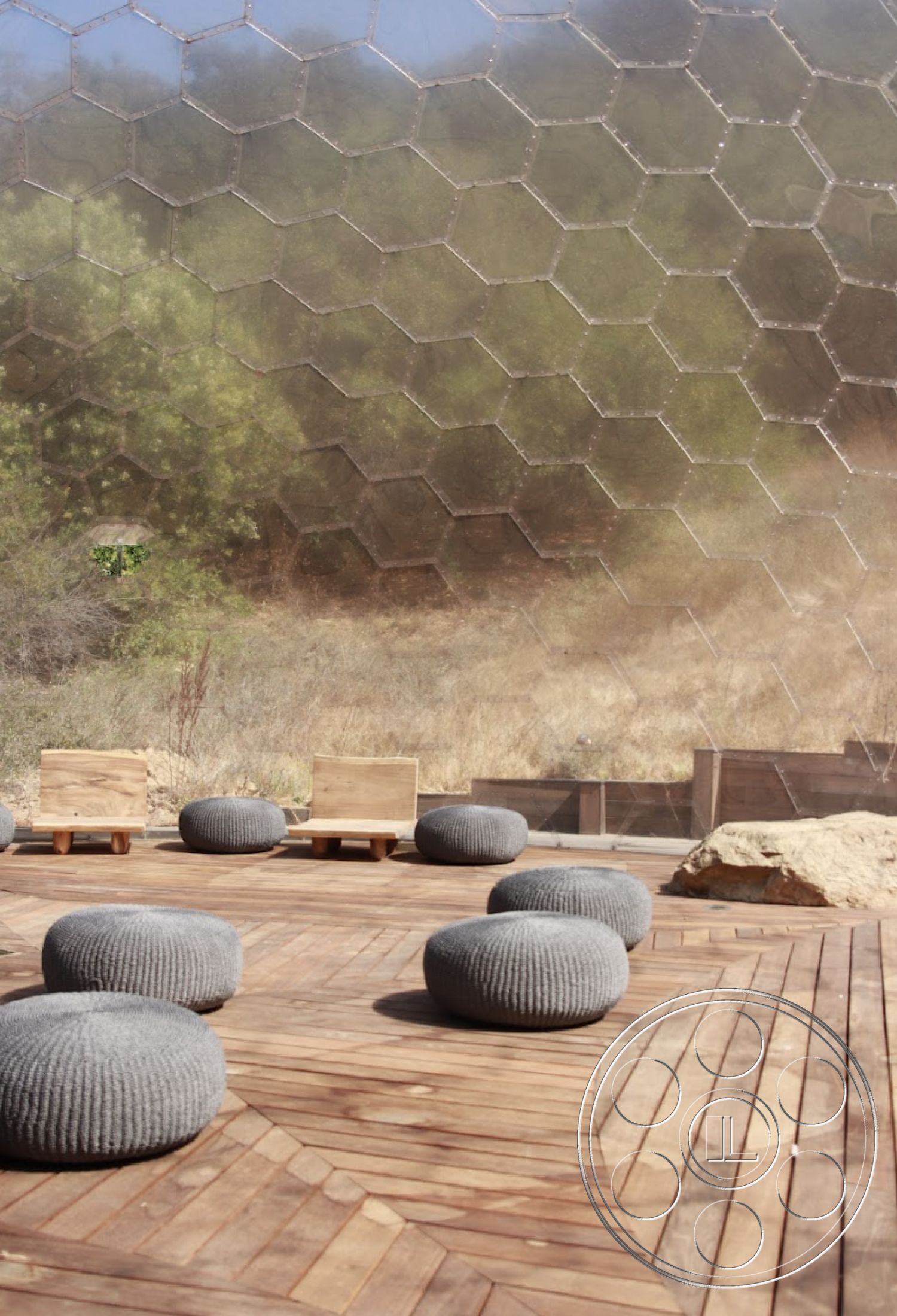 Topanga Retreat - outdoor seating area, wood deck flooring, interior outdoor space, natural rock features, hexagonal glass wall, textured knit poufs, minimalist wooden chairs, hexagonal architectural design, modern environment setting, rustic landscape backdrop