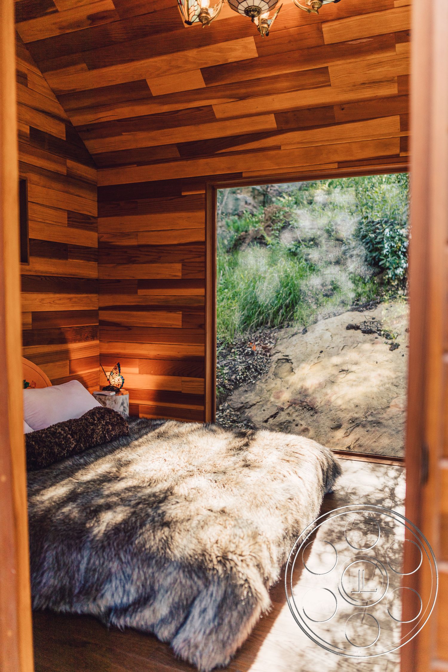 Topanga Retreat - interior natural light, interior hardwood flooring, interior rustic decor, interior minimalist design, interior plush area rug, interior wood paneling walls, interior glass sliding door, interior decorative light fixture, interior nature view, interior soft bedding, interior cozy bedroom, interior sloped ceiling, interior wooden window frame, interior accent throw pillows, interior cabin-style aesthetic