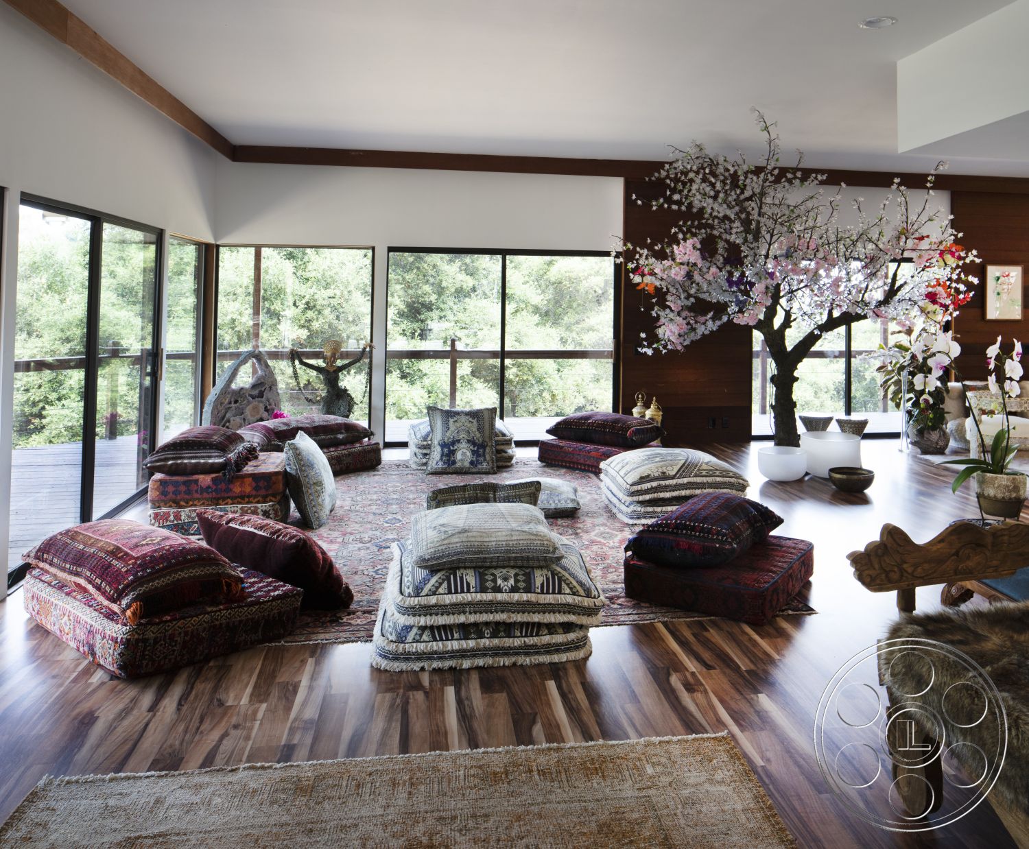 Topanga Retreat - neutral color palette, glass sliding doors, floor-to-ceiling windows, artistic wall decorations, decorative throw pillows, hardwood living room floors, minimalist furniture design, natural wood accent walls, open concept interior, textured area rugs, contemporary floor plan, cozy relaxation space, lush green outdoor view, modern upholstered seating, indoor flowering tree decor, low seating arrangement, sunny indoor ambiance, airy and bright interior, multi-purpose living area