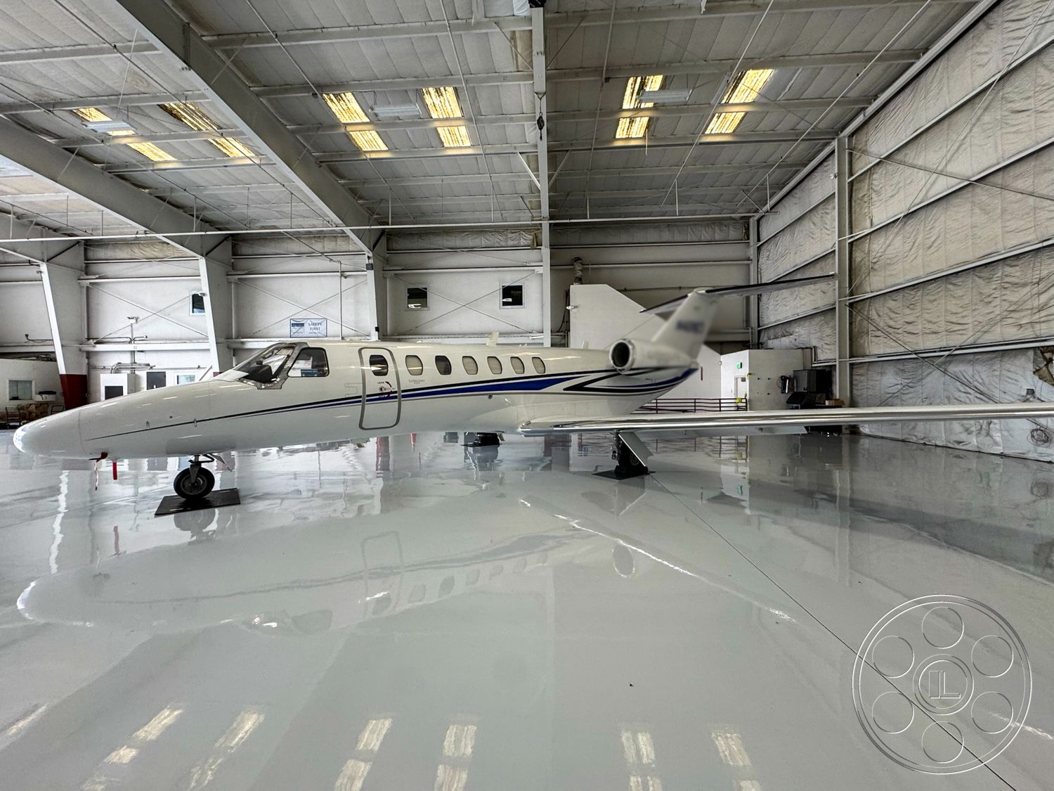 VN Hangar - concrete flooring, industrial lighting fixtures, high vaulted ceiling, ground-level access, open layout design, white wall treatment, insulated wall panels, aircraft storage space, aircraft maintenance area, aircraft hangar interior, sheet metal construction, glossy epoxy floor finish, large hangar doors, padded workstation areas, metal framework details