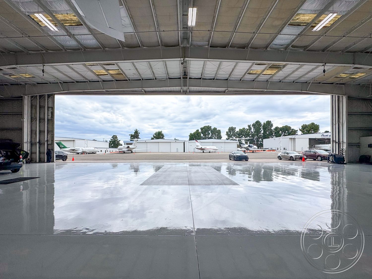 VN Hangar - open floor plan, industrial design elements, concrete floor finish, commercial lighting fixtures, high ceilings with exposed trusses, exterior aircraft hangar, metal frame structure, steel roof panels, glossy epoxy garage floor, large roll-up hangar door, vehicular access space, tarmac view, surrounding airstrip environment, airport runway perspective, hangar space for aviation