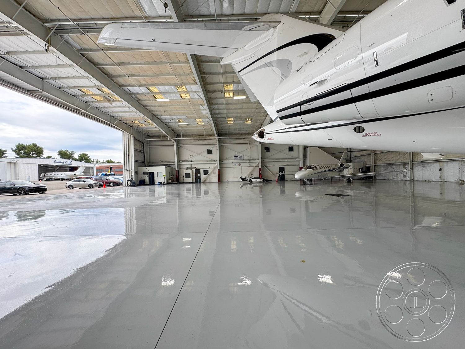 VN Hangar - open floor plan, concrete walls, functional workspace, tall ceiling, exposed steel structural beams, industrial ceiling lights, bright overhead lighting, aircraft maintenance space, large hangar doors, weather-resistant exterior, high gloss epoxy flooring, commercial airplane hangar, professional aviation setting, ventilation systems, dry hangar, automobile parking area