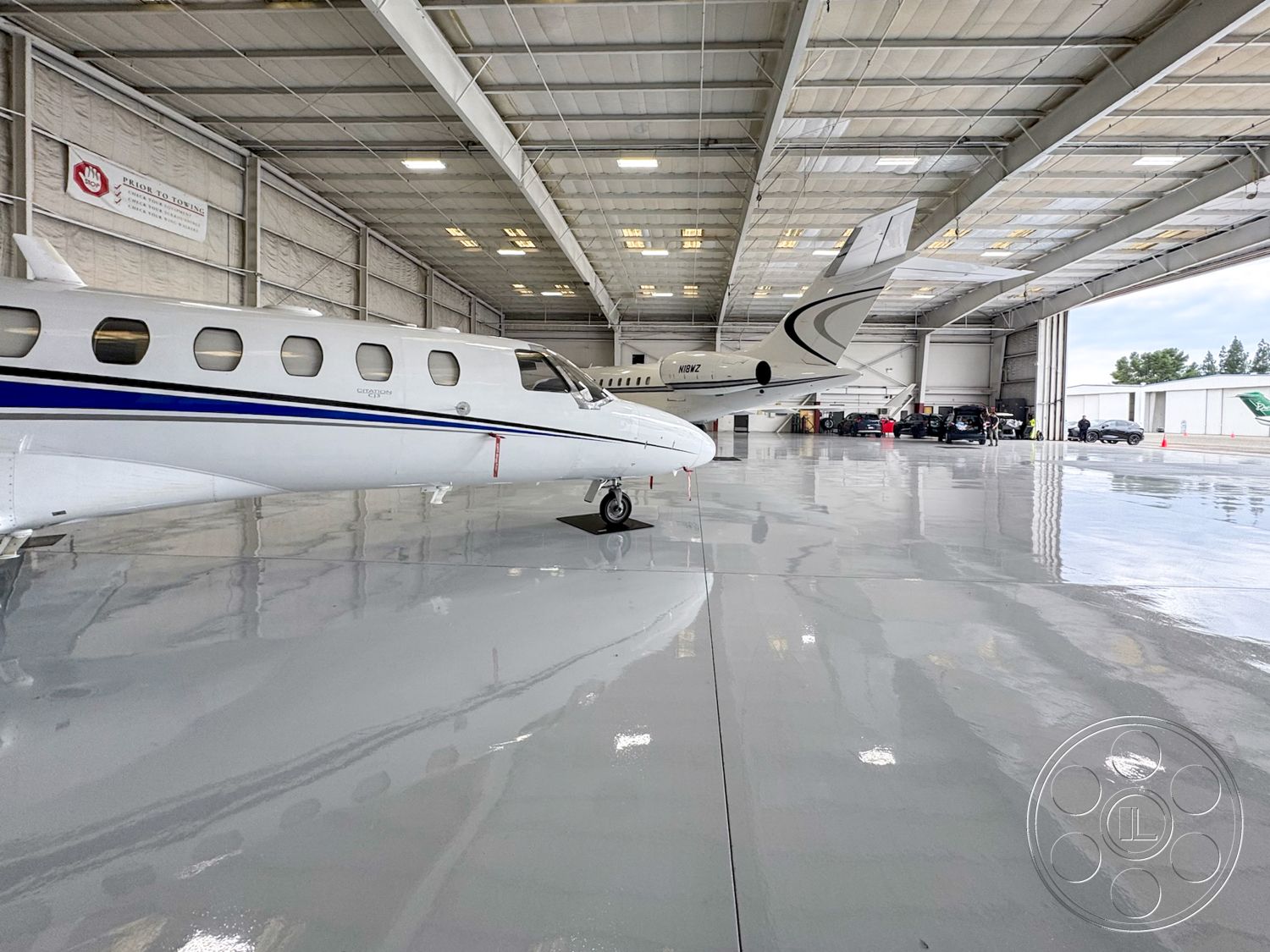 VN Hangar - open floor plan, large glass windows, overhead lighting fixtures, concrete slab foundation, epoxy garage floor, aircraft maintenance area, metal aircraft hangar exterior, high ceiling industrial space, painted steel structure, commercial hangar interior, insulated metal panels, service vehicle parking area, high bay doors, industrial ventilation system, reflective floor surface