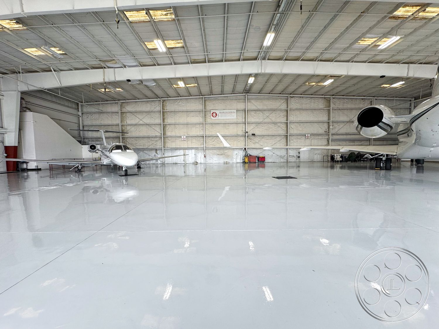 VN Hangar - floor-to-ceiling windows, white painted walls, glass entry doors, aircraft parking area, insulated wall panels, polished concrete hangar floor, metal truss ceiling structure, high ceilings with industrial lighting, expansive interior space, engineered steel frame construction, substantial hangar doors, exposed ductwork for HVAC, elevated administrative area, open layout for aircraft servicing, heavy-duty overhead lighting, fire safety systems integration, smooth surface for aircraft movement, contemporary industrial hangar design, interior space with unobstructed sightlines