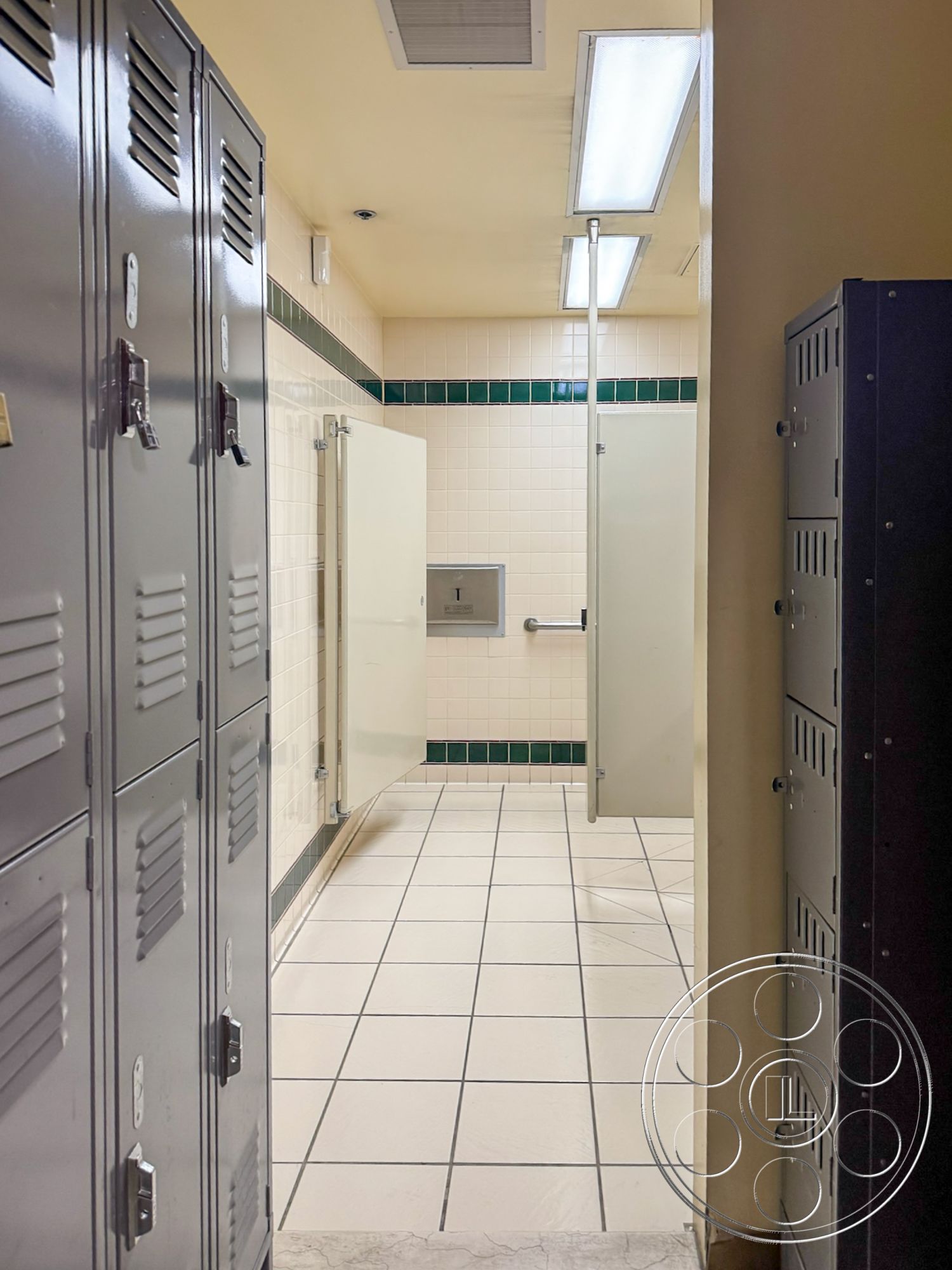 VN Hangar - neutral wall color, accessibility features, changing area, rectangular shower area, functional restroom design, interior locker room, metal lockers with gray finish, white ceramic wall tiles, green tile accent strip, white grid tile flooring, glass shower partitions, fluoresent ceiling lights, vending machine area, modern locker room facilities