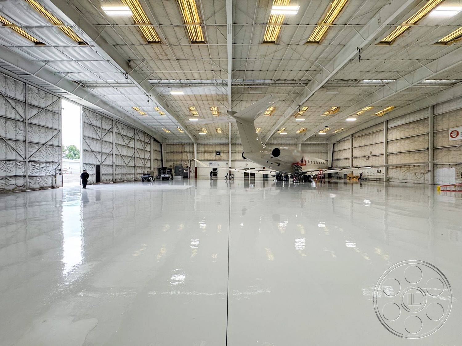VN Hangar - open space layout, industrial lighting fixtures, suspended ceiling grid, insulated wall panels, epoxy floor coating, metal frame structure, high ceiling hangar space, reflective concrete flooring, large airplane hangar, exterior overhead doors, textured drywall finish, sealed concrete surfaces, commercial aircraft maintenance, clear-span construction, heavy-duty door systems, ventilation ductwork