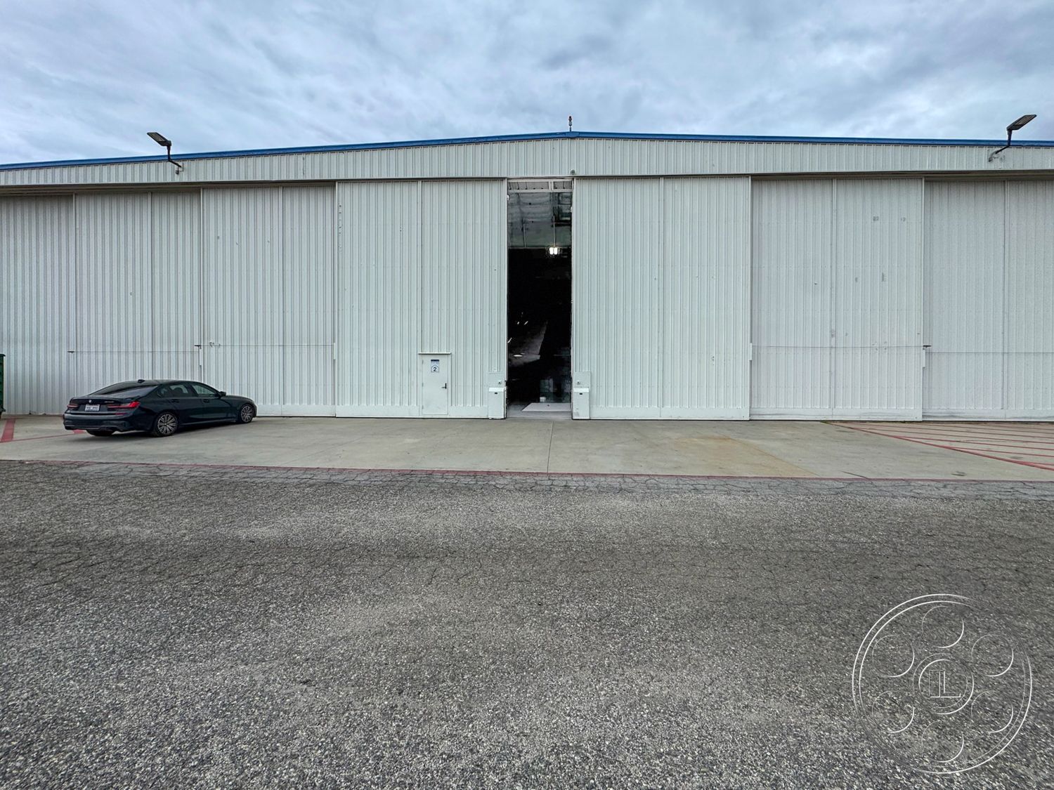 VN Hangar - outdoor lighting fixtures, asphalt parking lot, flat roof design, urban commercial setting, concrete loading dock, exposed steel frame, large roll-up doors, metal exterior cladding, industrial warehouse structure, high-ceiling space, rectangular building form, interior loading area, exterior service entrance, surrounding concrete pavement, adjacent vehicle parking, functional utilitarian architecture