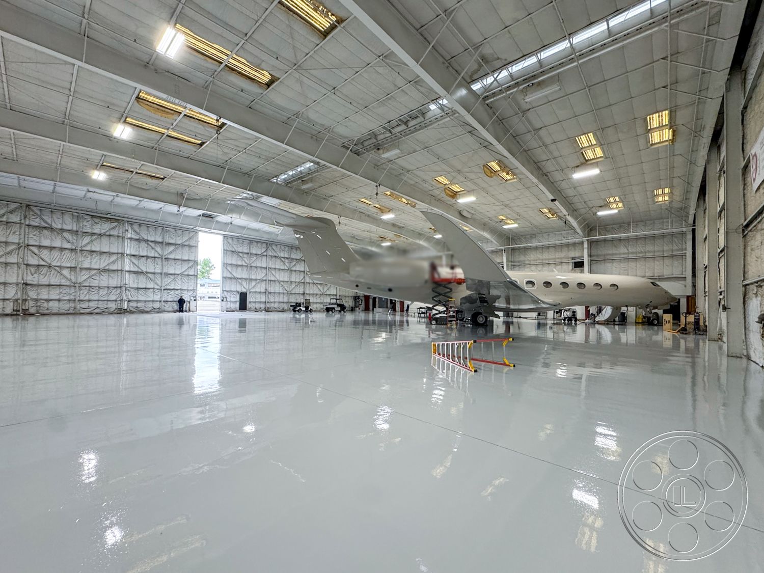 VN Hangar - floor-to-ceiling windows, industrial lighting fixtures, adjacent parking area, modern industrial design, steel frame construction, large roll-up doors, exterior aircraft hangar, epoxy-coated concrete floor, reflective floor surface, high-ceilinged interior, insulated panel walls, glossy concrete flooring, wide-open space, mechanical maintenance area, office space within hangar, elevated work platform, metal beam ceiling structure, outdoor tarmac view